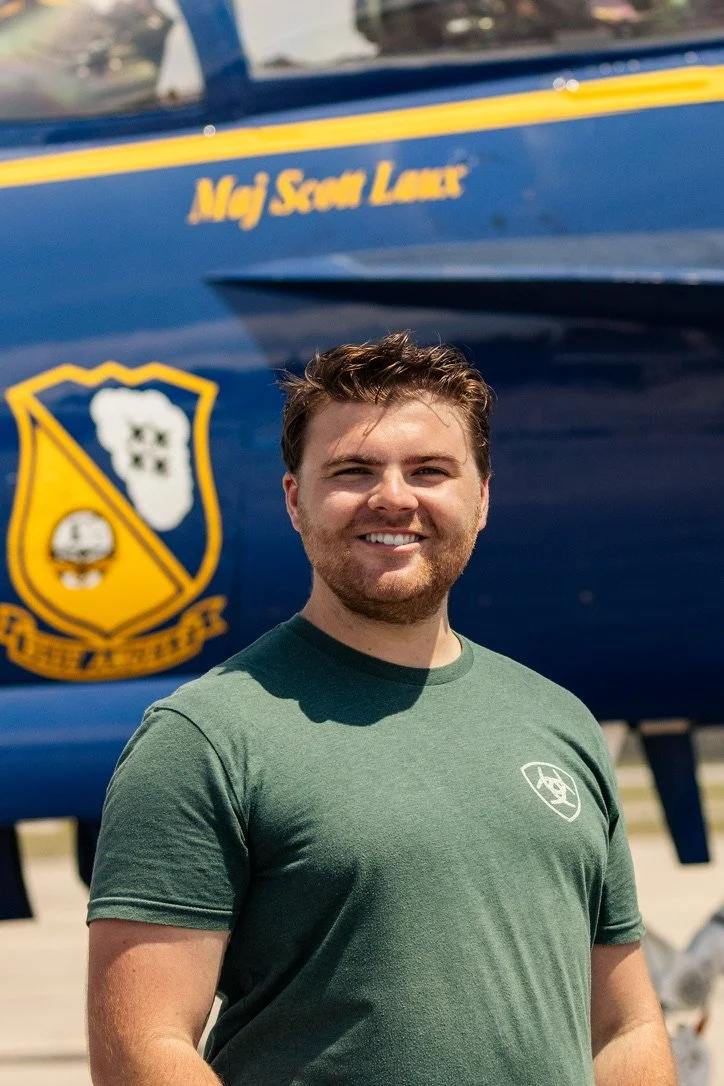 A young man smiling in front of a Blue Angel.
