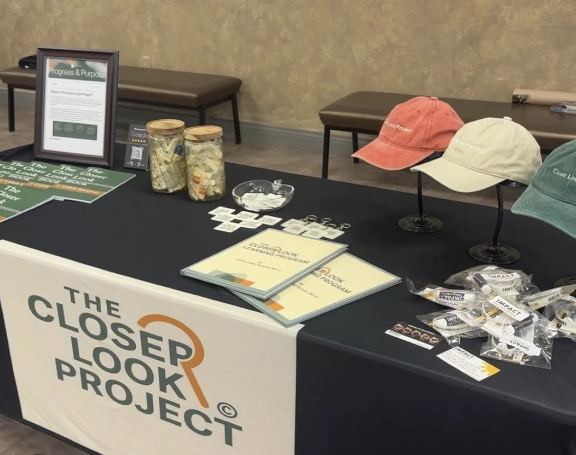 Table display for The Closer Look Project with brochures, hats, and jars of recovered items.