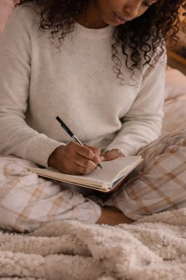 Woman sitting with a notebook, journaling to process emotions and reduce stress in a peaceful space.