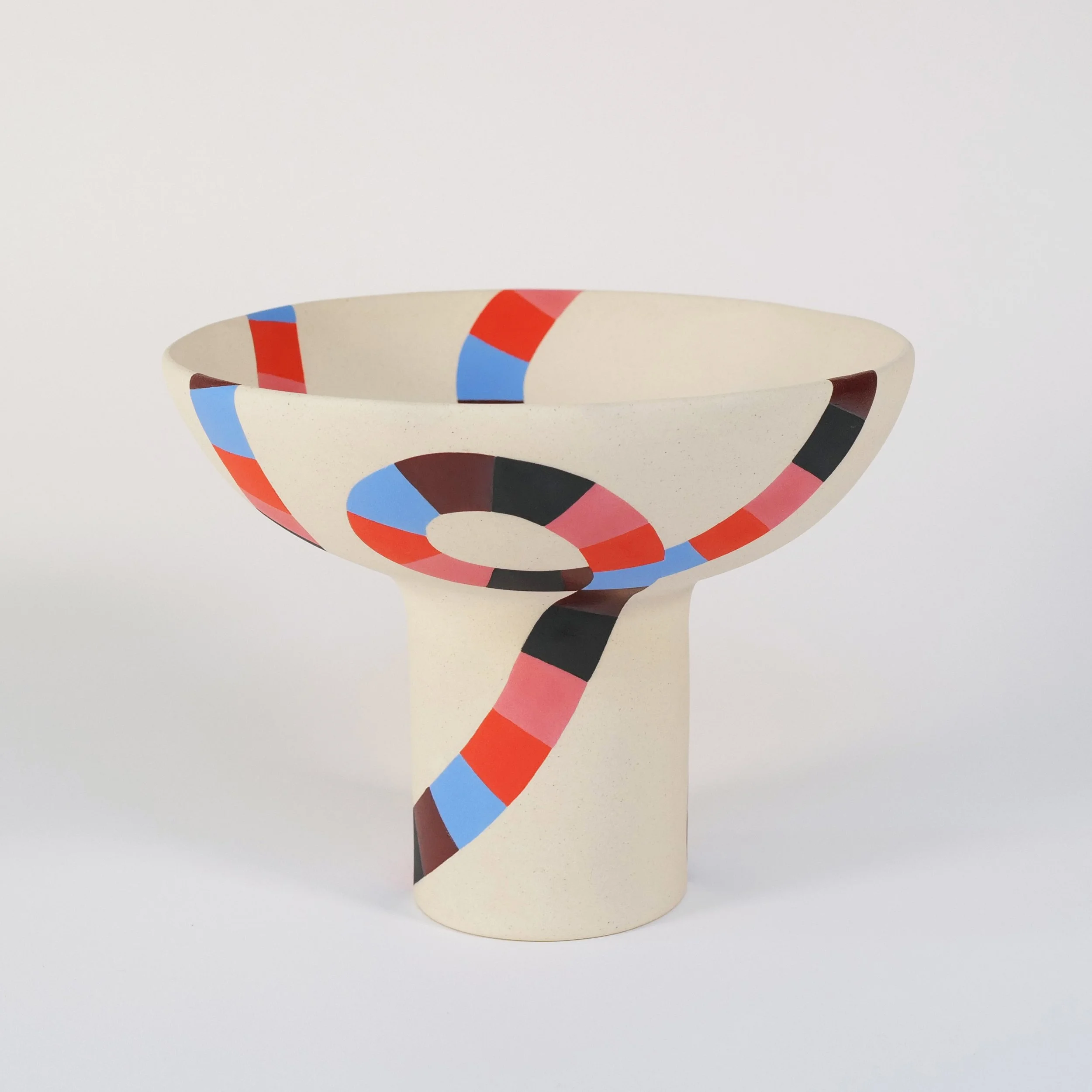A ceramic bowl with a wide, shallow shape and a pedestal base, decorated with colorful, geometric multicolor pattern, set on a white background.