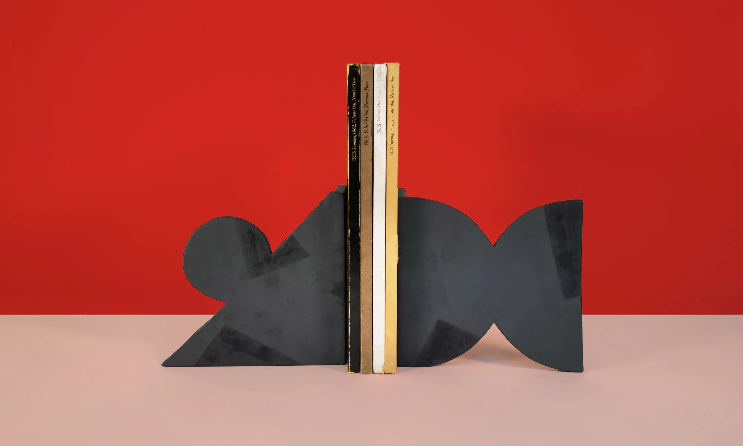 A set of black asymmetrical bookends on either side of a set of books. The background is red and pale pink.