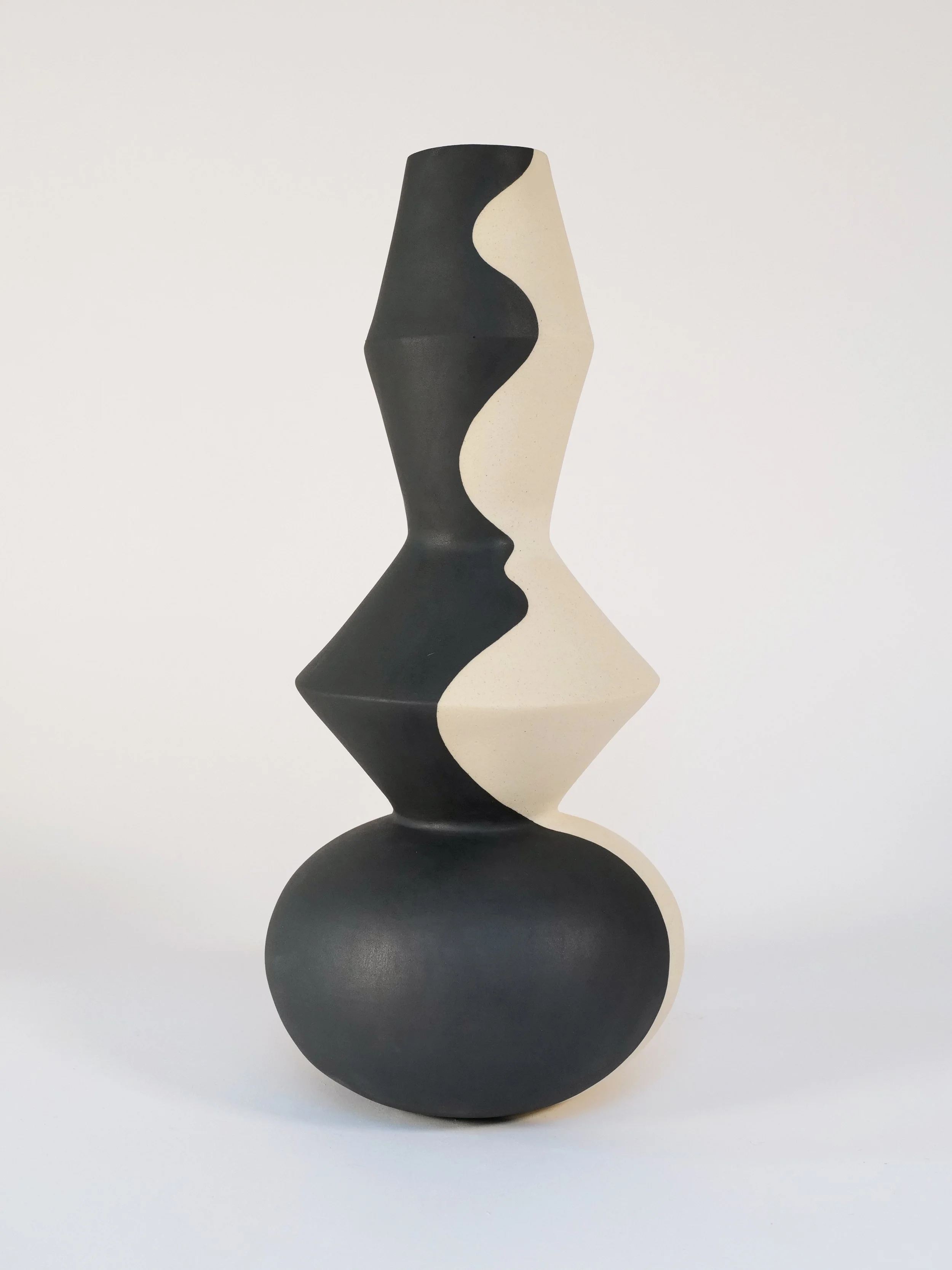 Abstract black and white ceramic vase with a geometric hand-painted wave design on a white background.