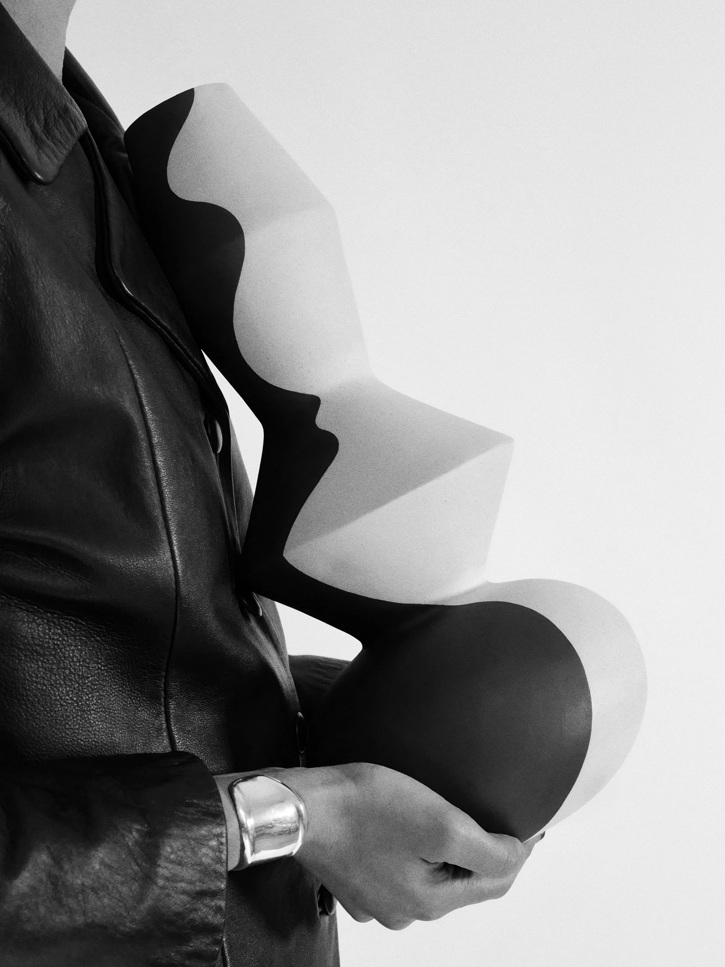 A person wearing a leather jacket holding a ceramic large vessel with a hand-painted abstract black and white wave pattern.