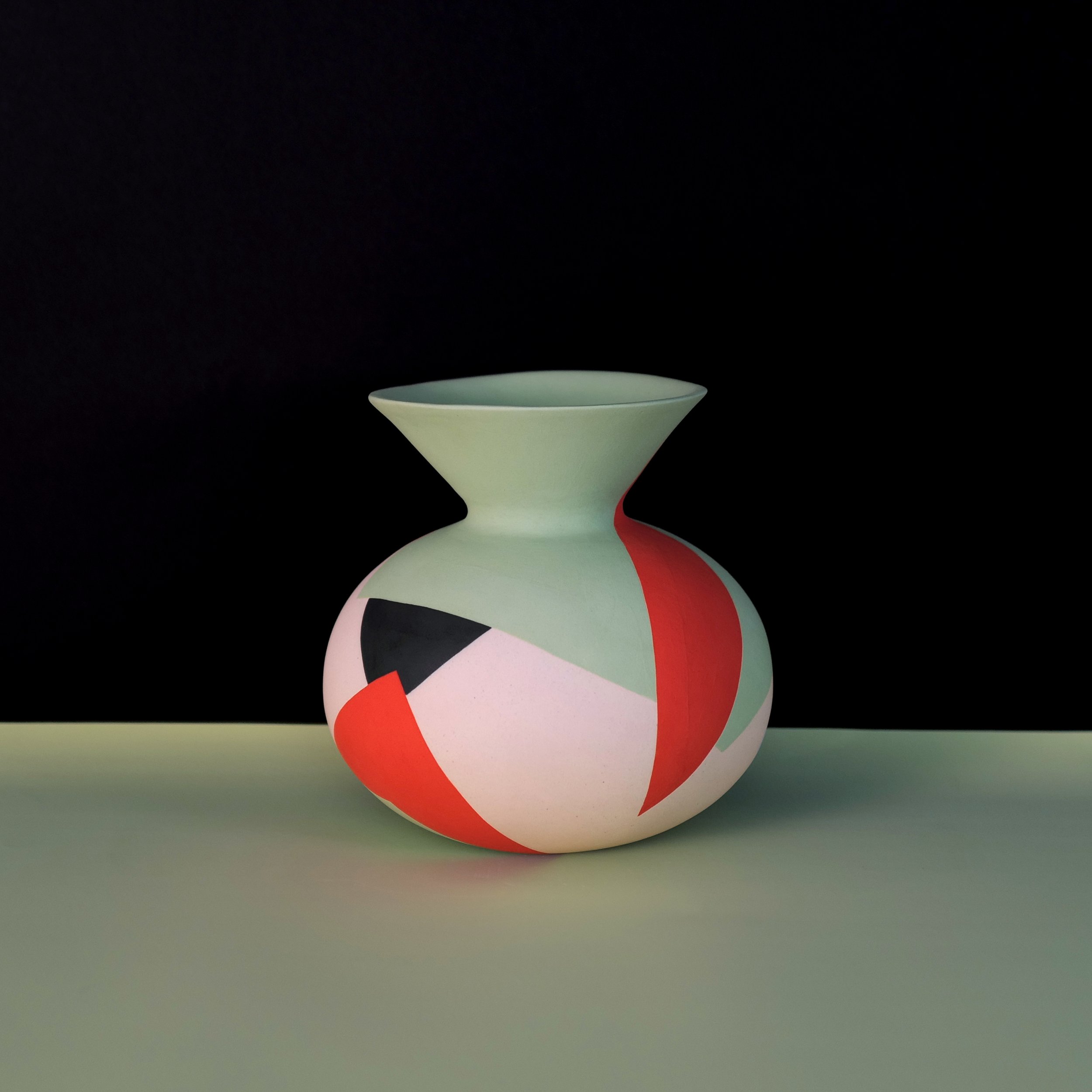 Colorful geometric ceramic vase with shapes in orange-red, black, white, and mint green, set against a black and green background.