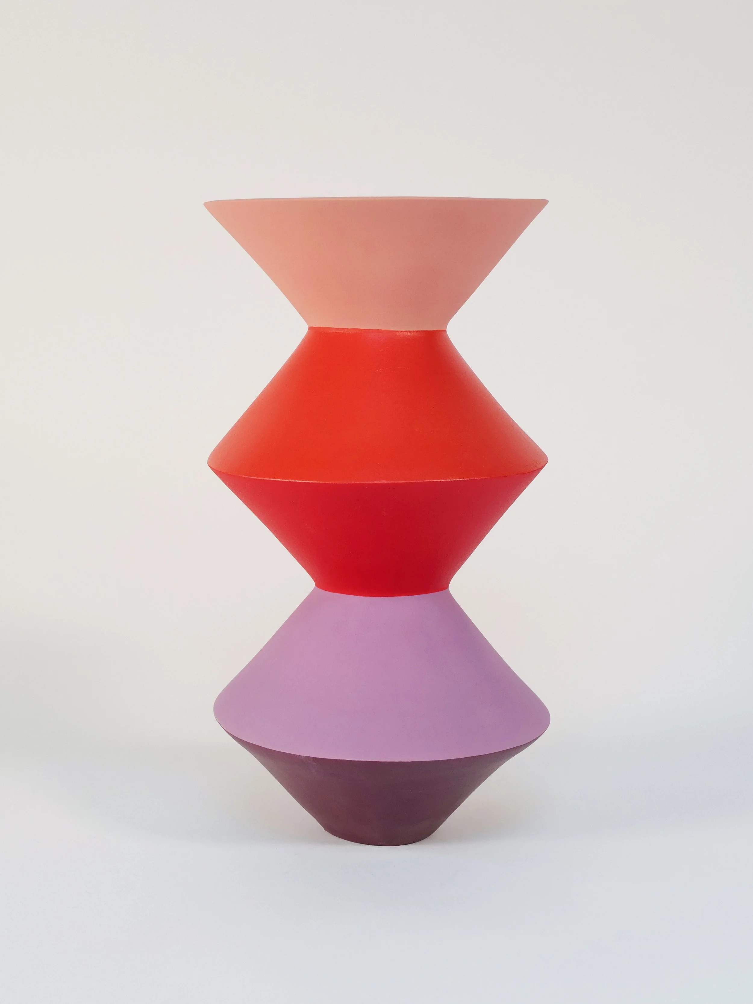 A zigzag-shaped vase composed of three stacked, conical shapes in pastel pink, orange-red, red, violet, and dark purple colors, set against a white background.
