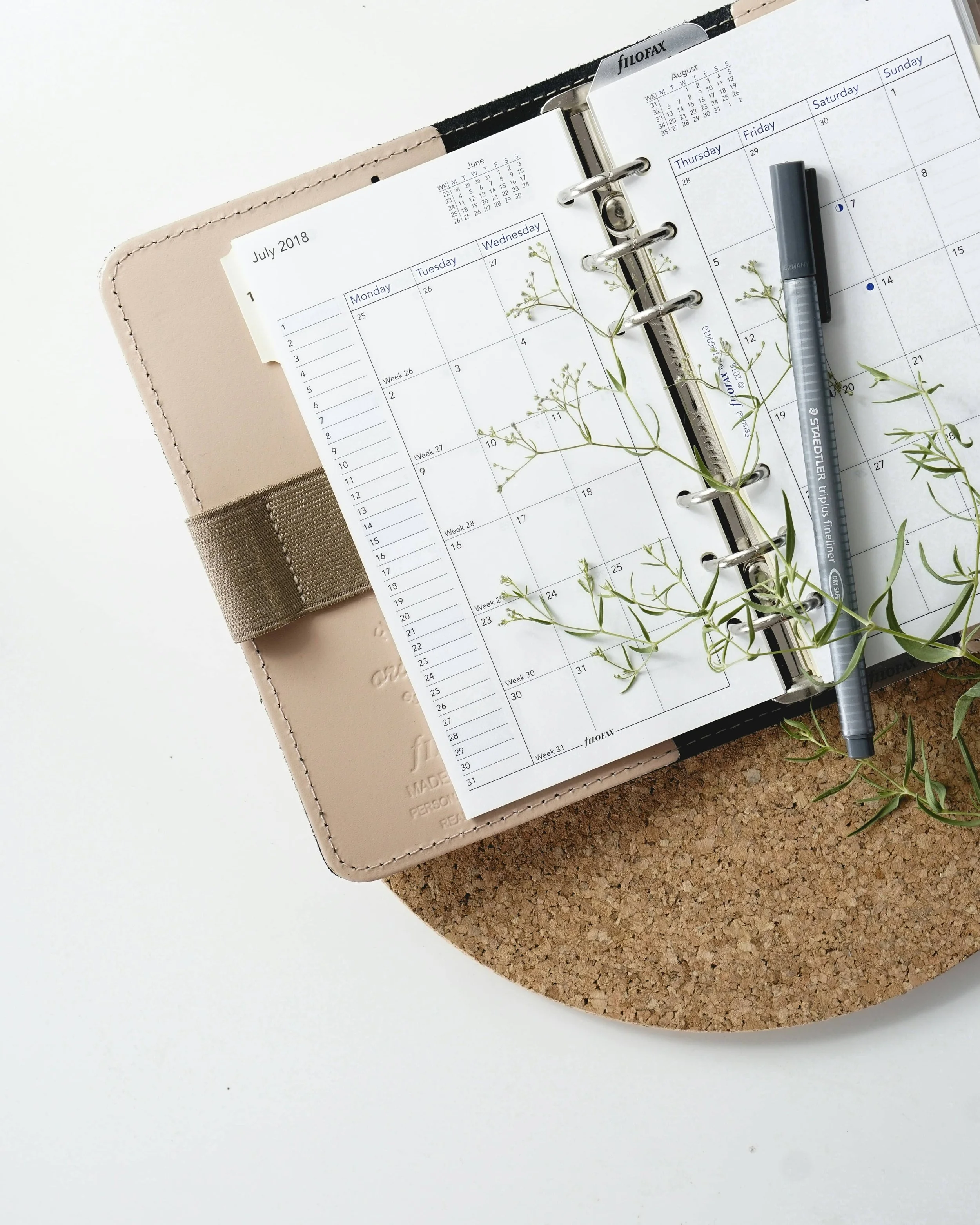 Open ring-bound planner showing a monthly calendar layout on a cork board with small green sprigs