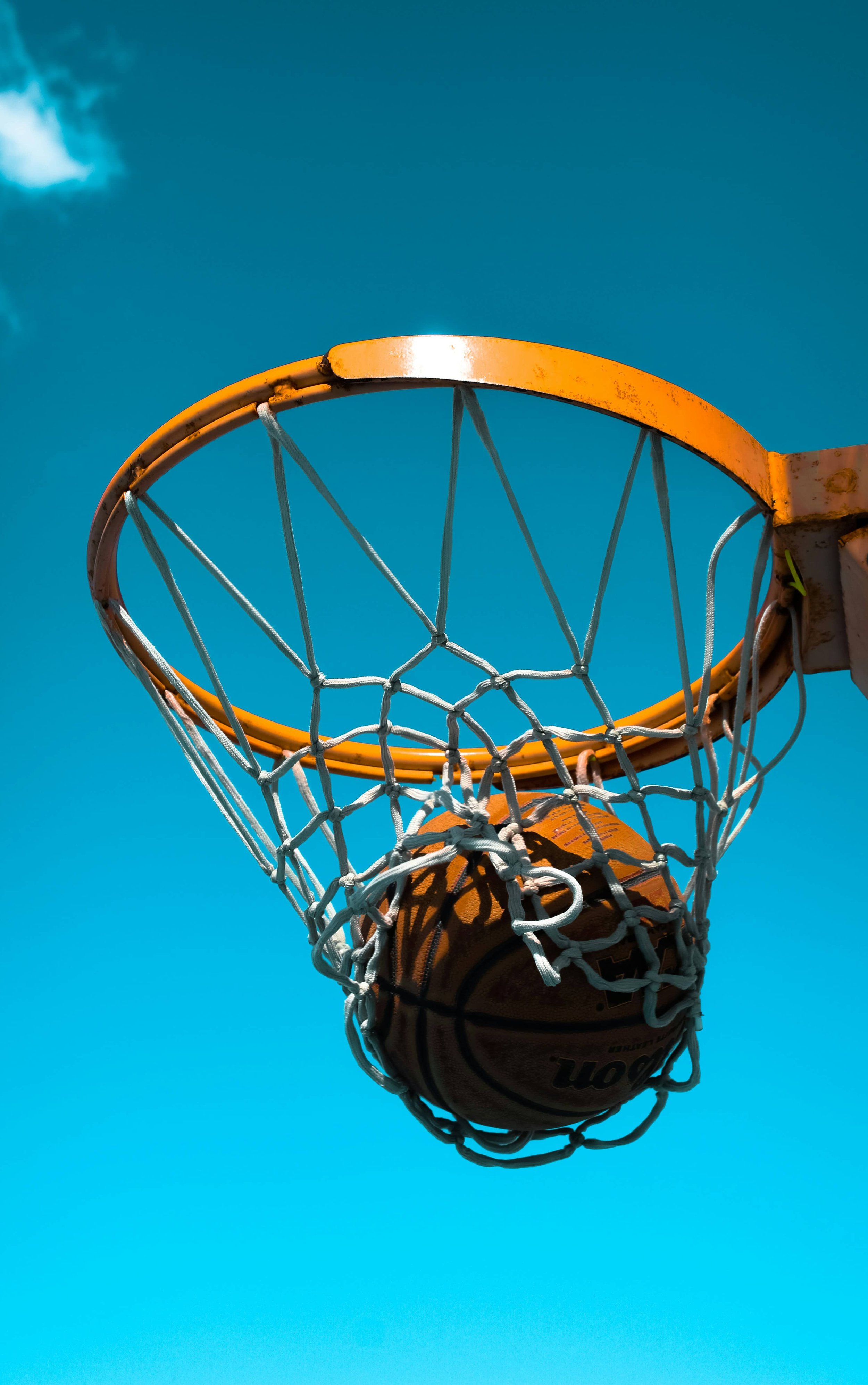 Basketball falling through an orange hoop and net viewed from below against a clear blue sky