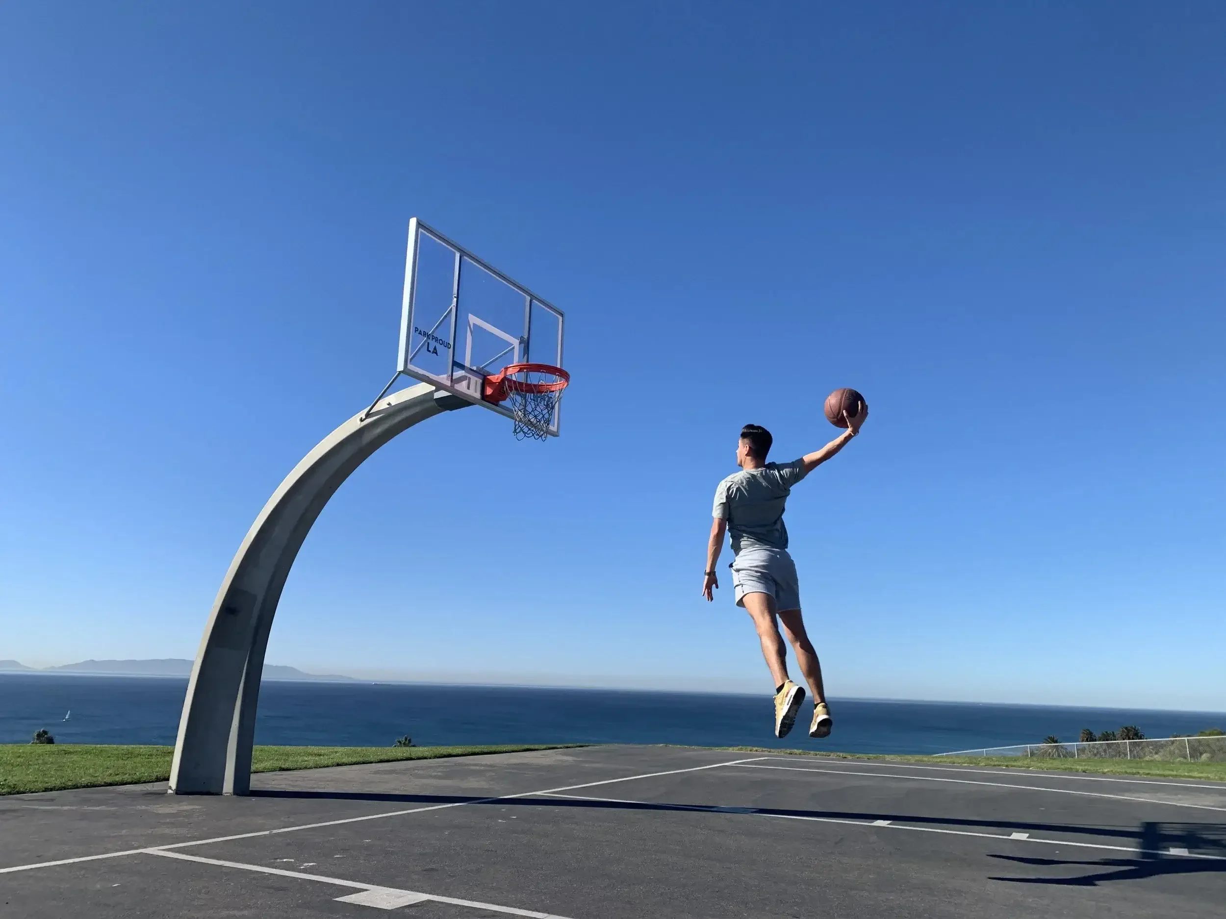 Kevin Sundin mid-air attempting a dunk on an oceanside basketball court under clear blue sky
