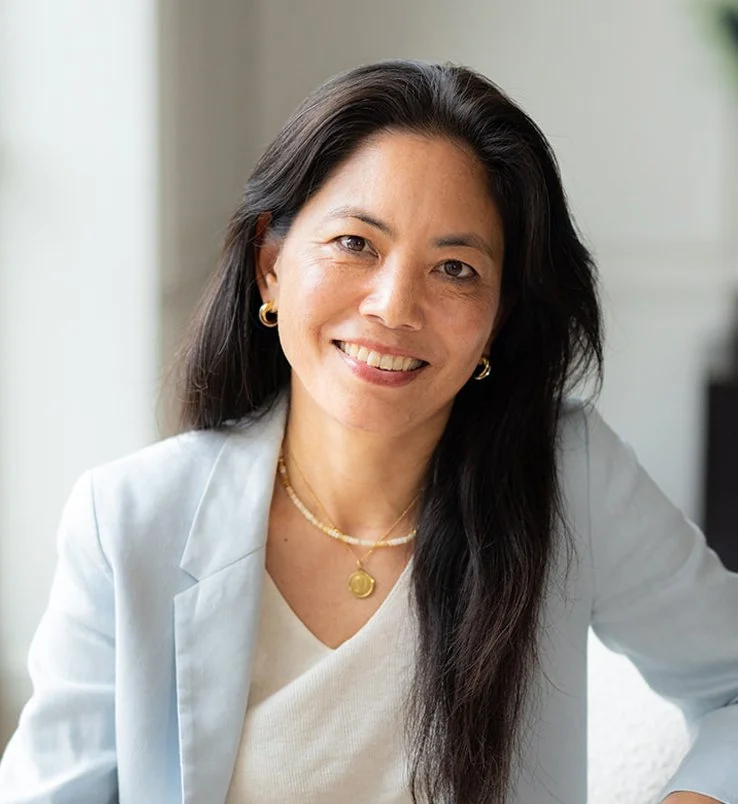 Mémé Watanabe, nutritional therapist, with long black hair smiling, wearing a blue blazer and gold jewelry