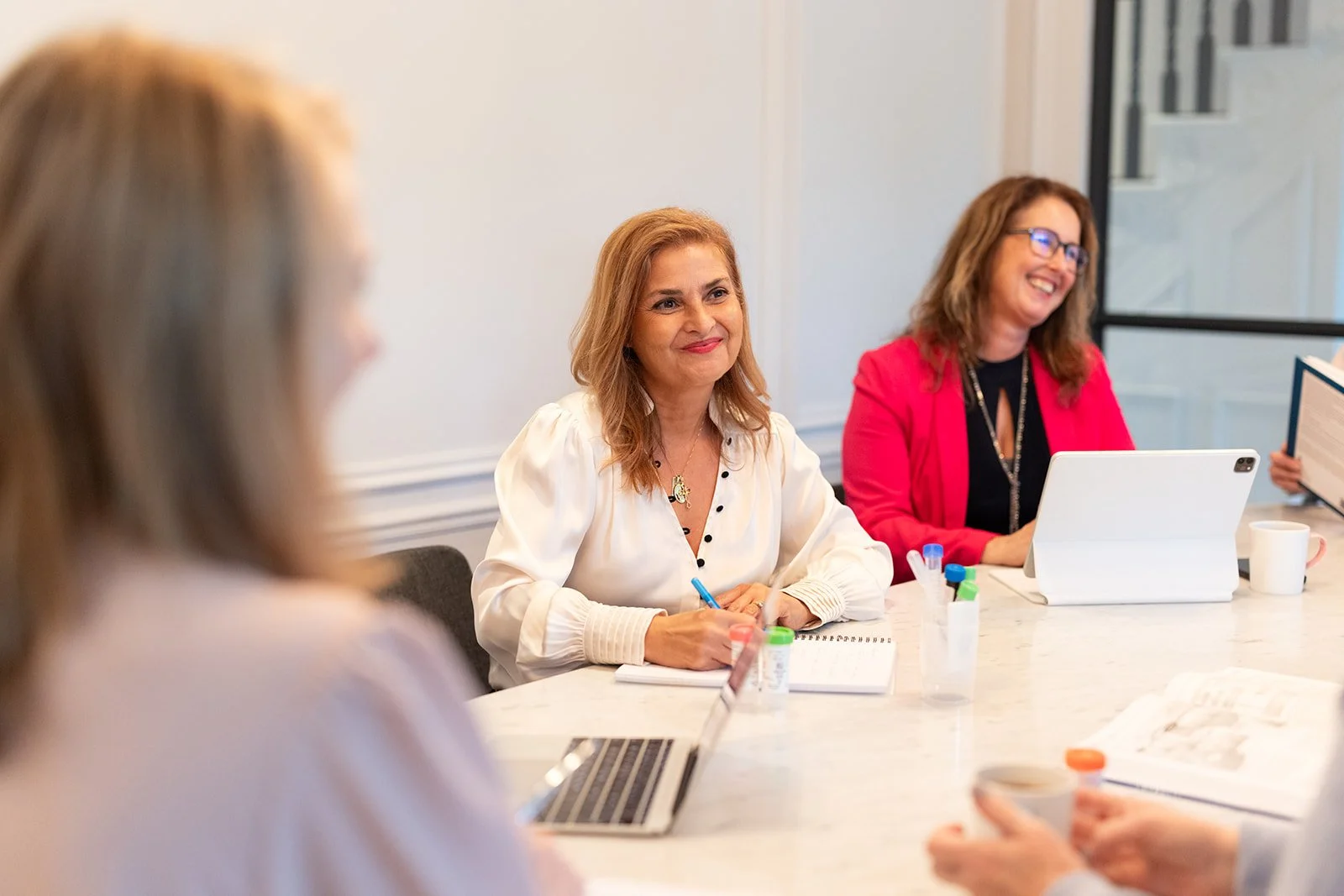 Group of specialists and nutritional therapists in a meeting room, smiling, with laptops, and coffee cups on the table.