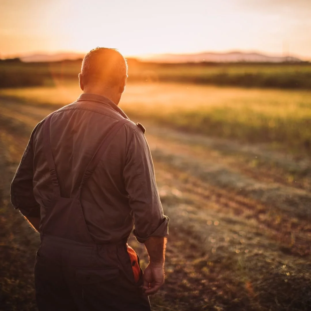 A man in a brown jacket walking in a field during sunset.