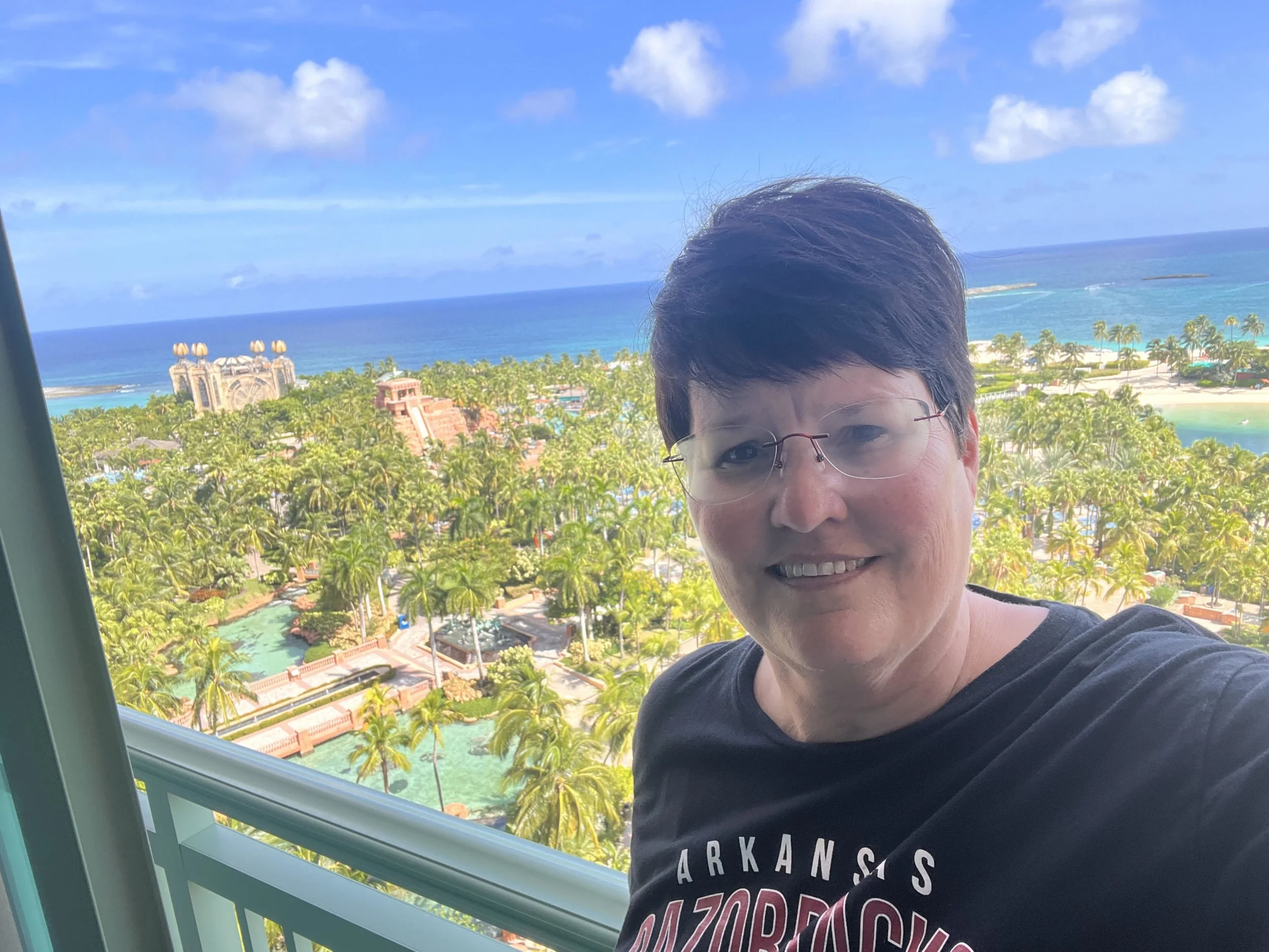 Person taking a selfie with a tropical resort and ocean view in the background.