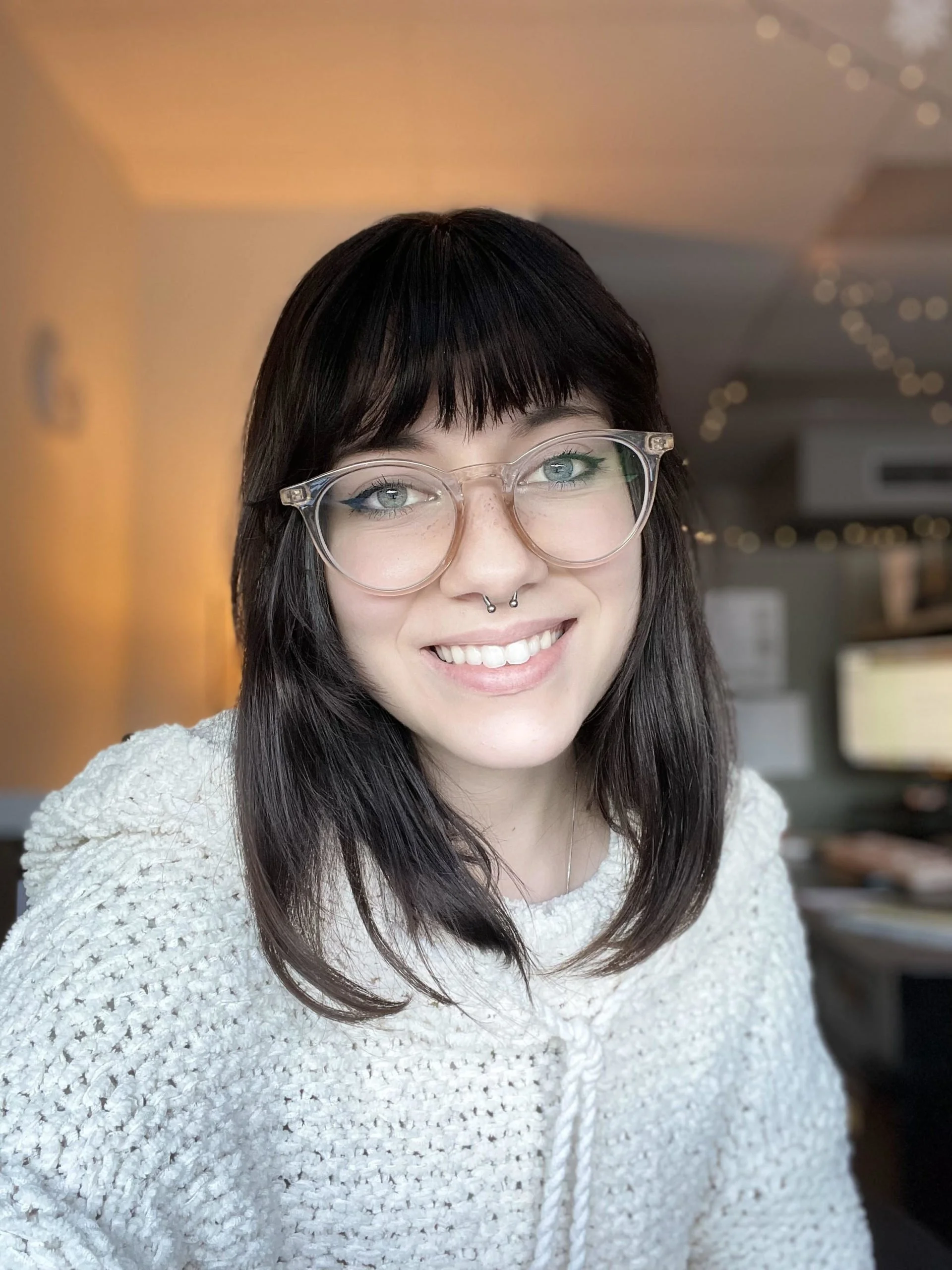 A young woman with dark hair and glasses smiling in an indoor setting.