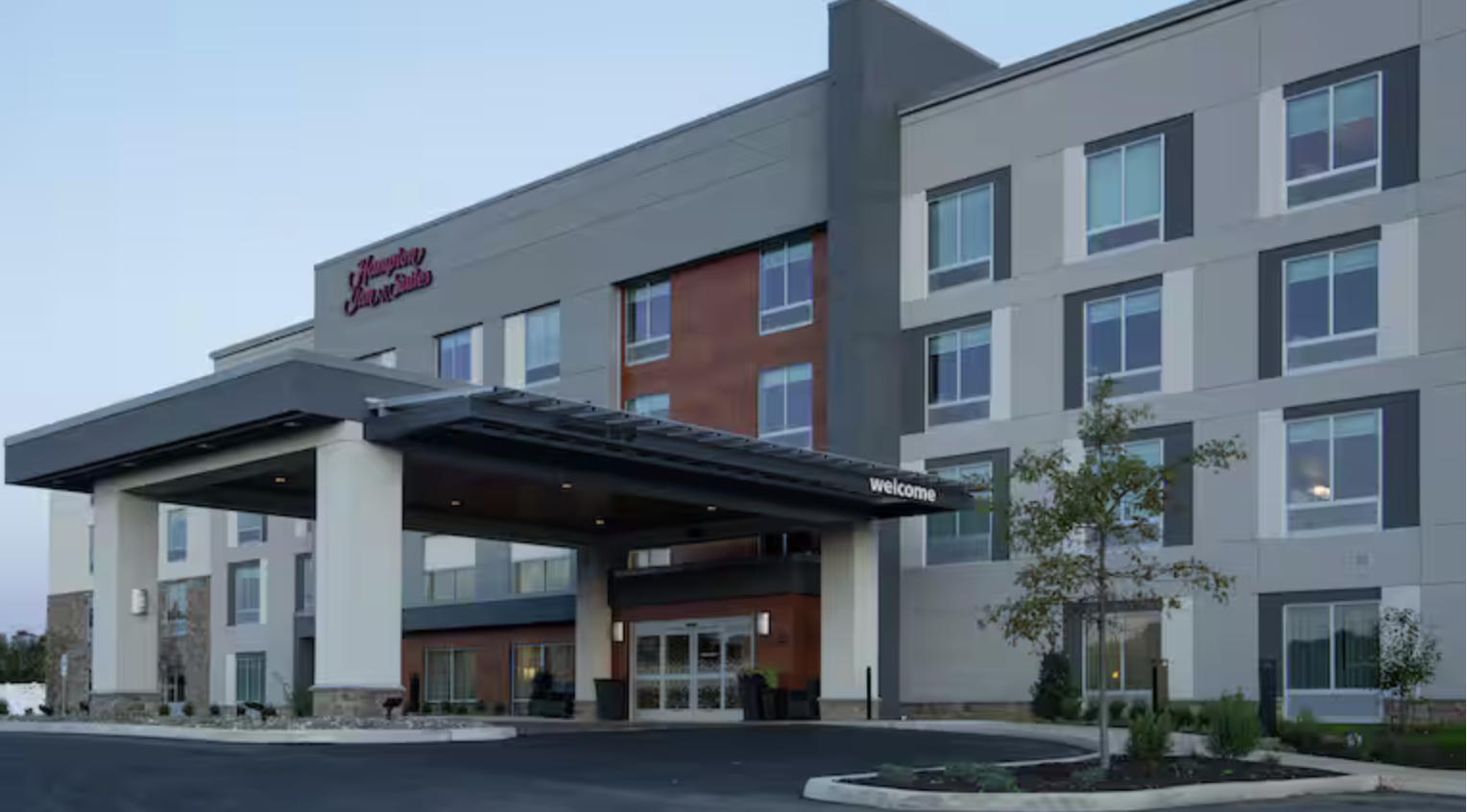Exterior of a modern hotel building with a welcoming entrance and signage that reads 'Hampton Inn & Suites.'