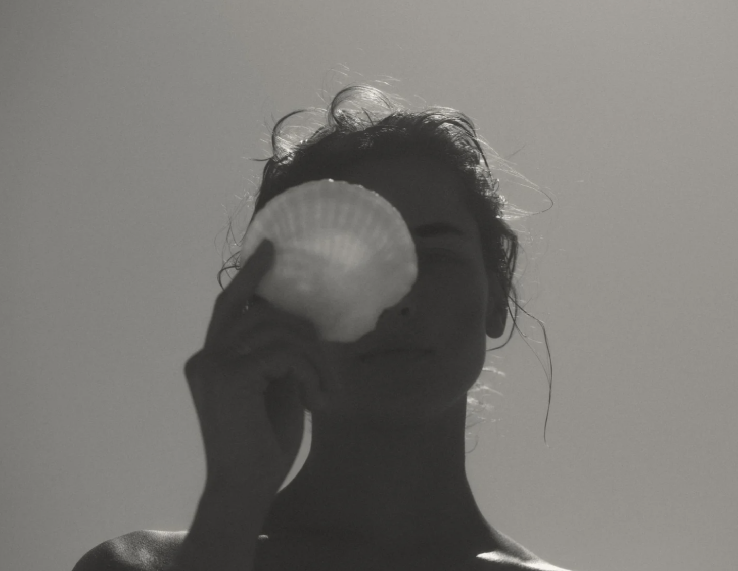 A person holding a seashell up to their face, with their silhouette visible against a plain background.