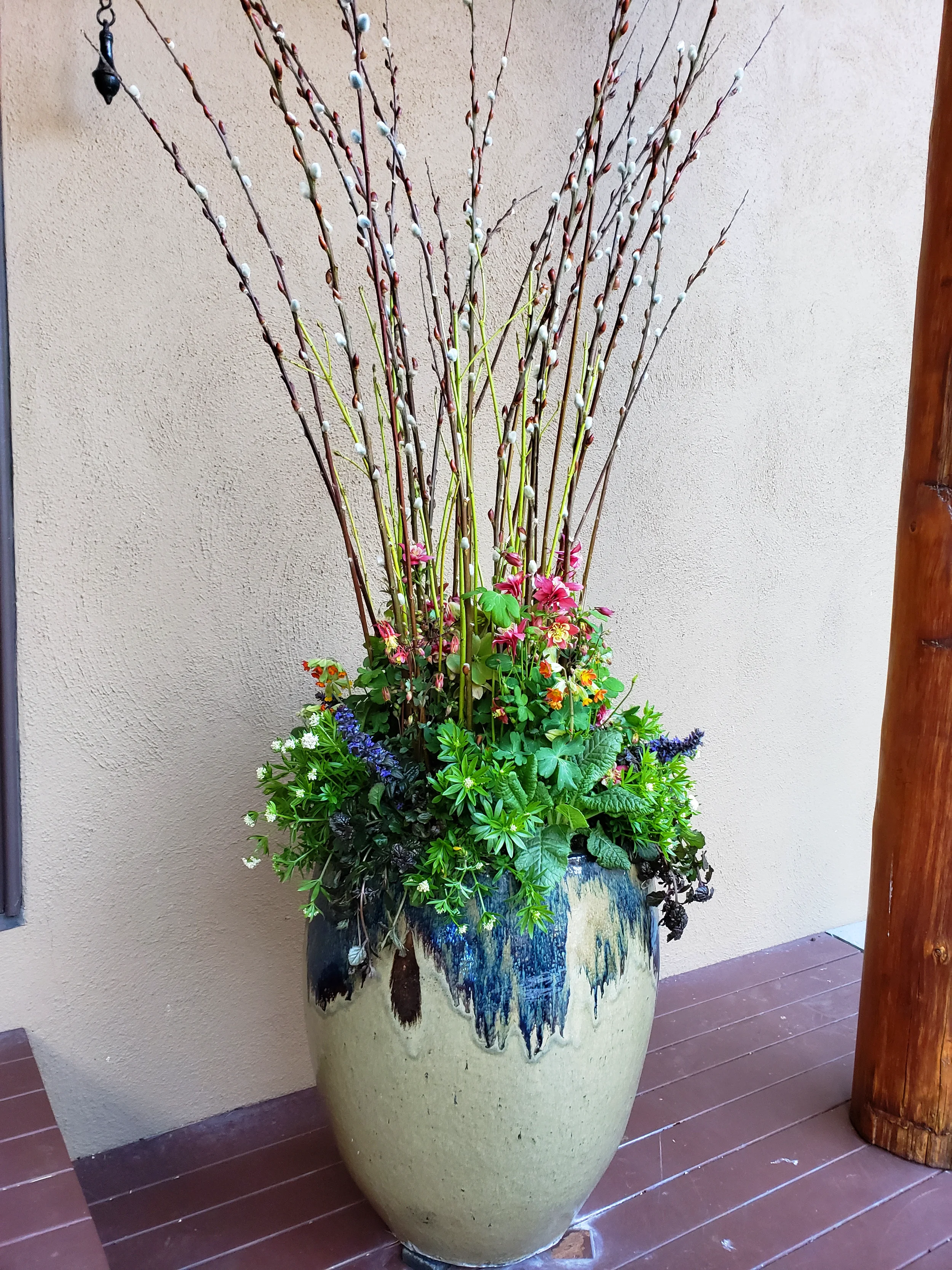 Large container design arrangement with budding branches and colorful flowers in a ceramic planter on a wooden floor.