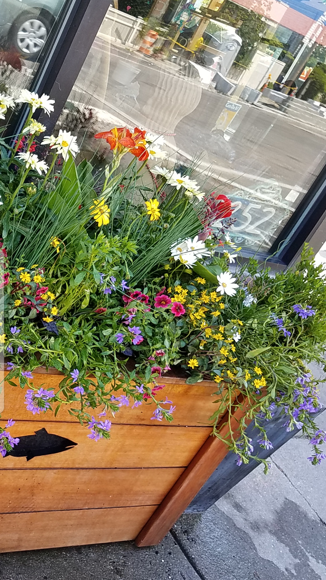 A wooden planter filled with colorful flowers such as daisies, petunias, and lilies outside a shop window.