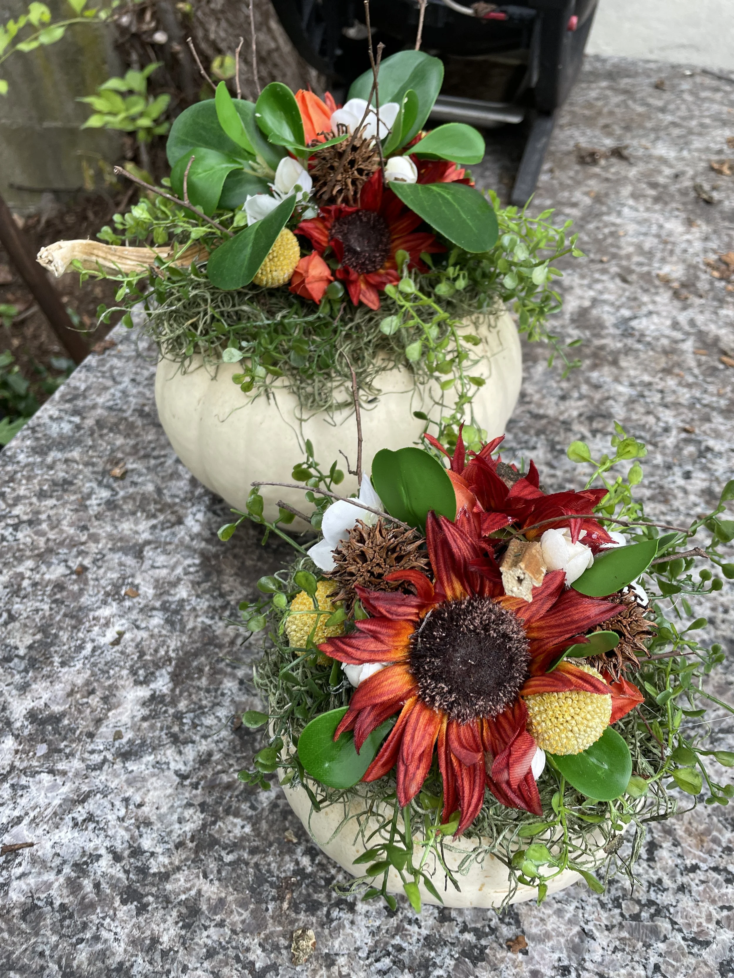 Two small flower arrangements with red, white, yellow, and orange flowers and green leaves on a stone surface outdoors.