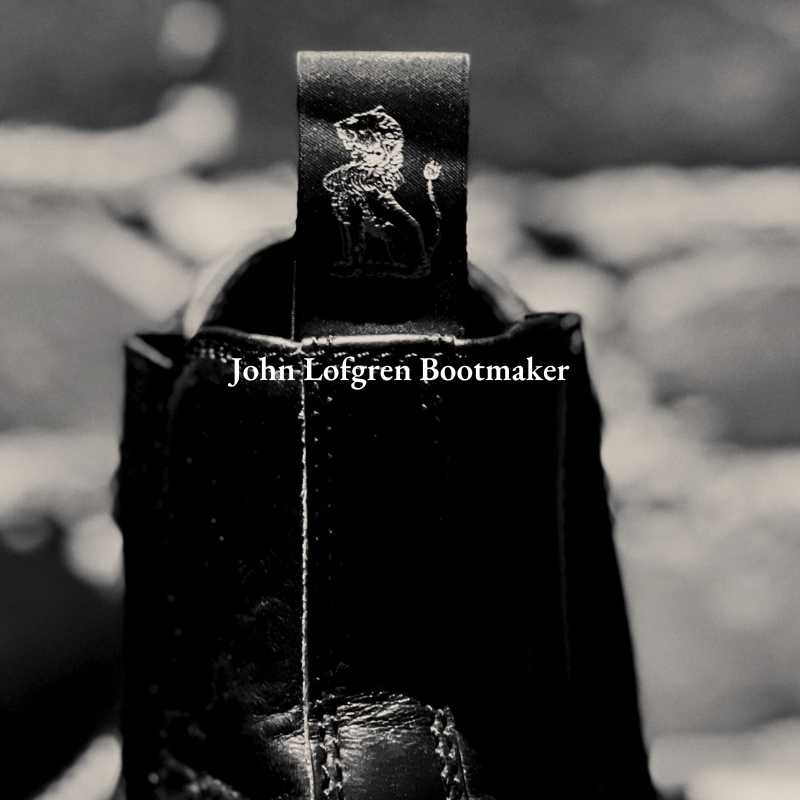 Close-up of a black leather boot with a label that reads 'John Lofgren Bootmaker' featuring a lion and crown logo.