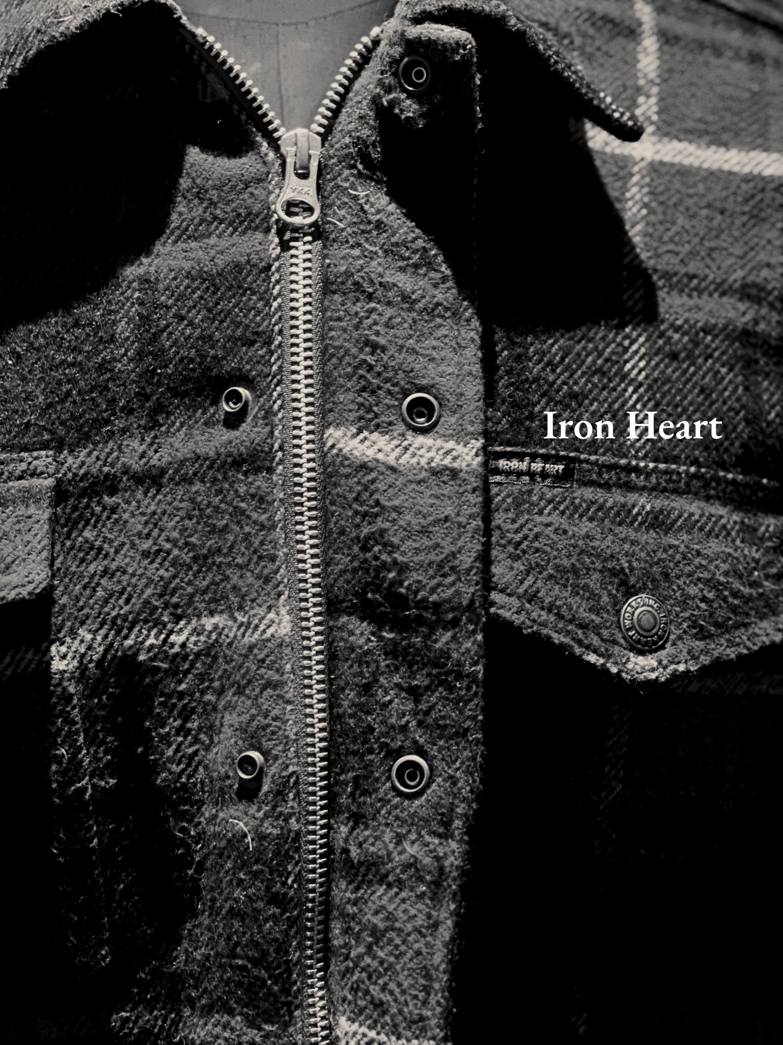 Black and white close-up of a textured jacket with a zipper in the center, a collar, and the words 'Iron Heart' embroidered on the right side.
