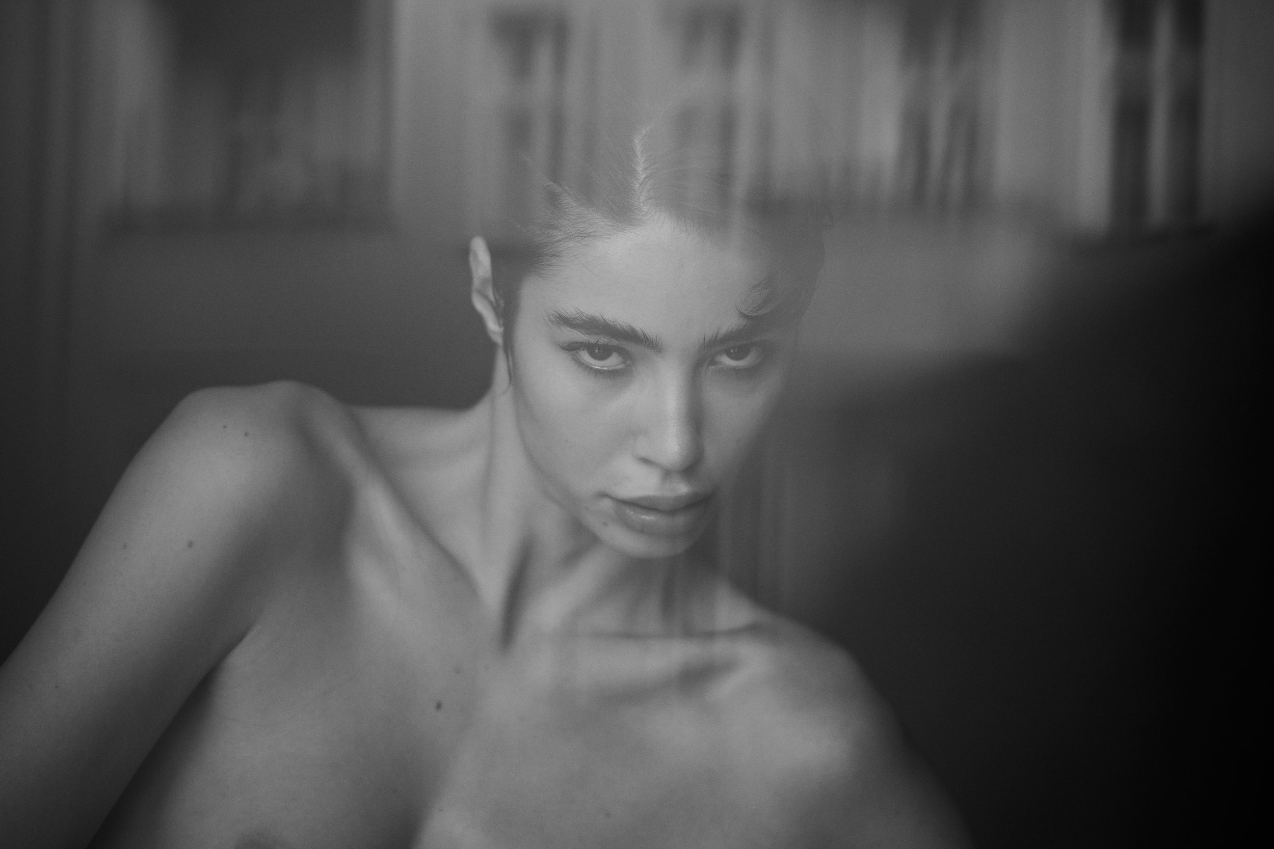 Schwarz-weiß-Foto einer nackten Frau mit dunklen Haaren, das auf einer Seite liegt und den Blick direkt in die Kamera richtet.