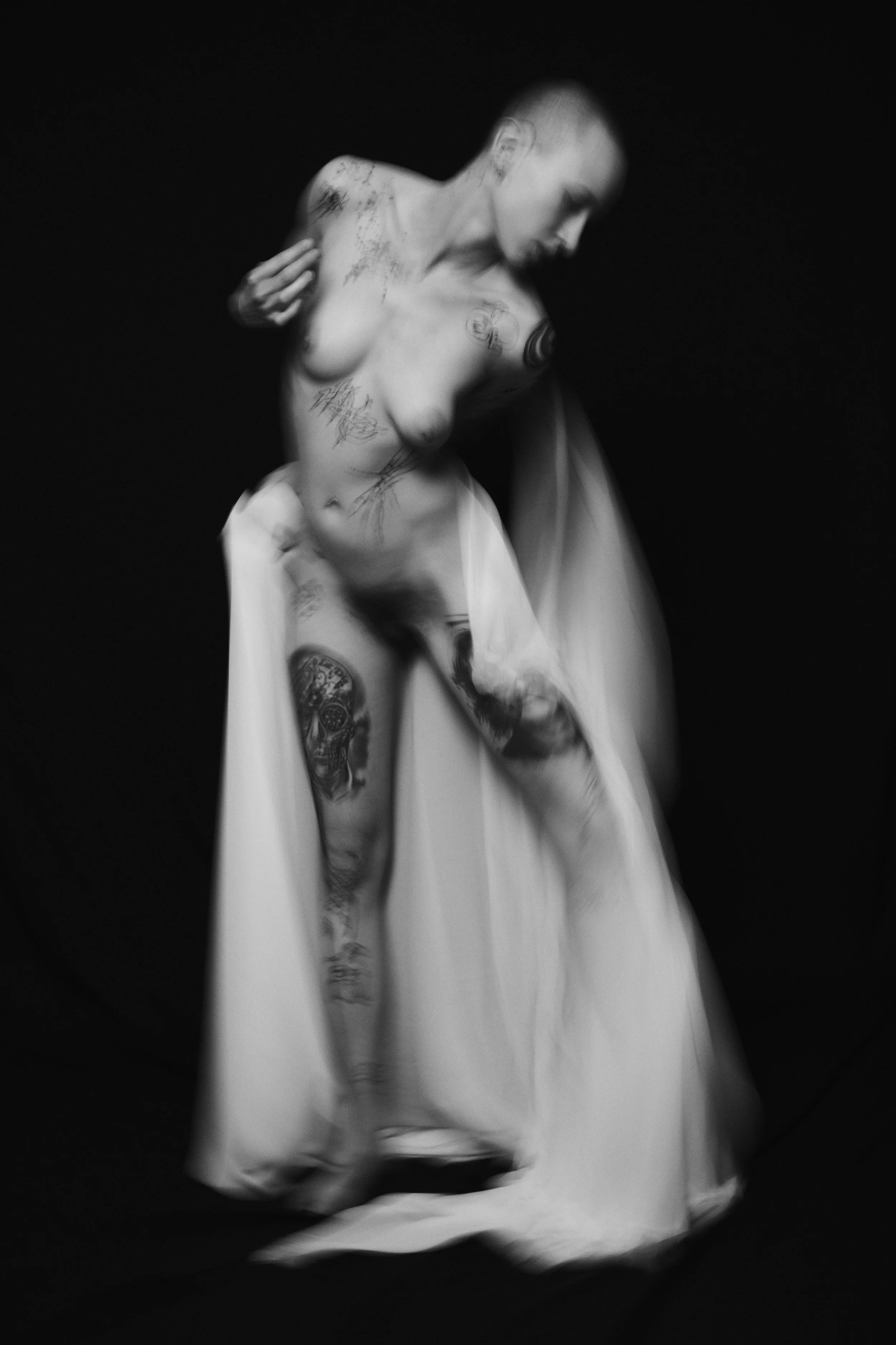 Schwarz-weiß-Foto eines nackten Menschen mit Tattoos, der eine weiße Hose trägt, bewegend vor einem schwarzen Hintergrund.