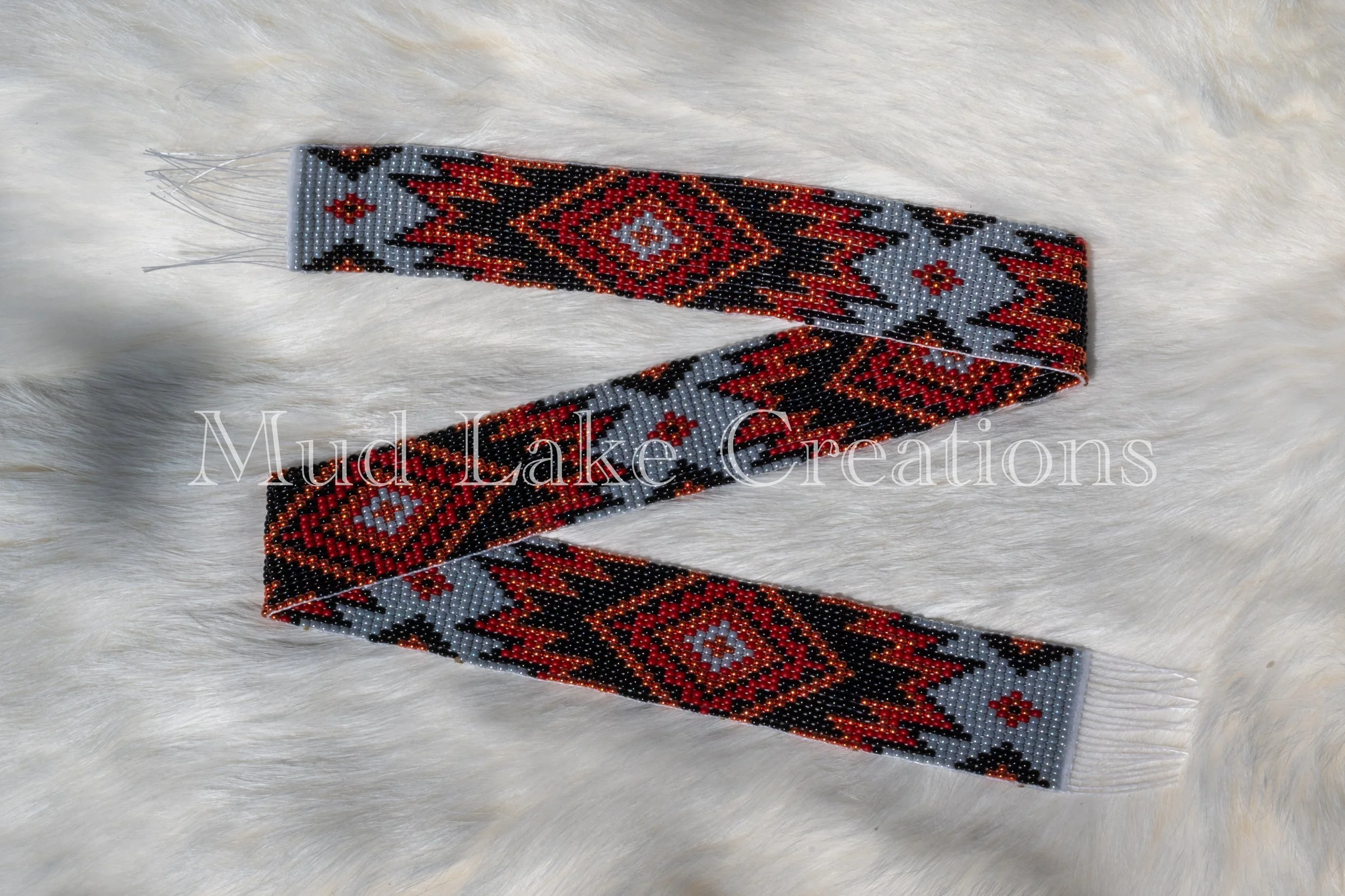 A beaded bracelet with geometric patterns in red, black, and gray on a soft, white, furry surface.
