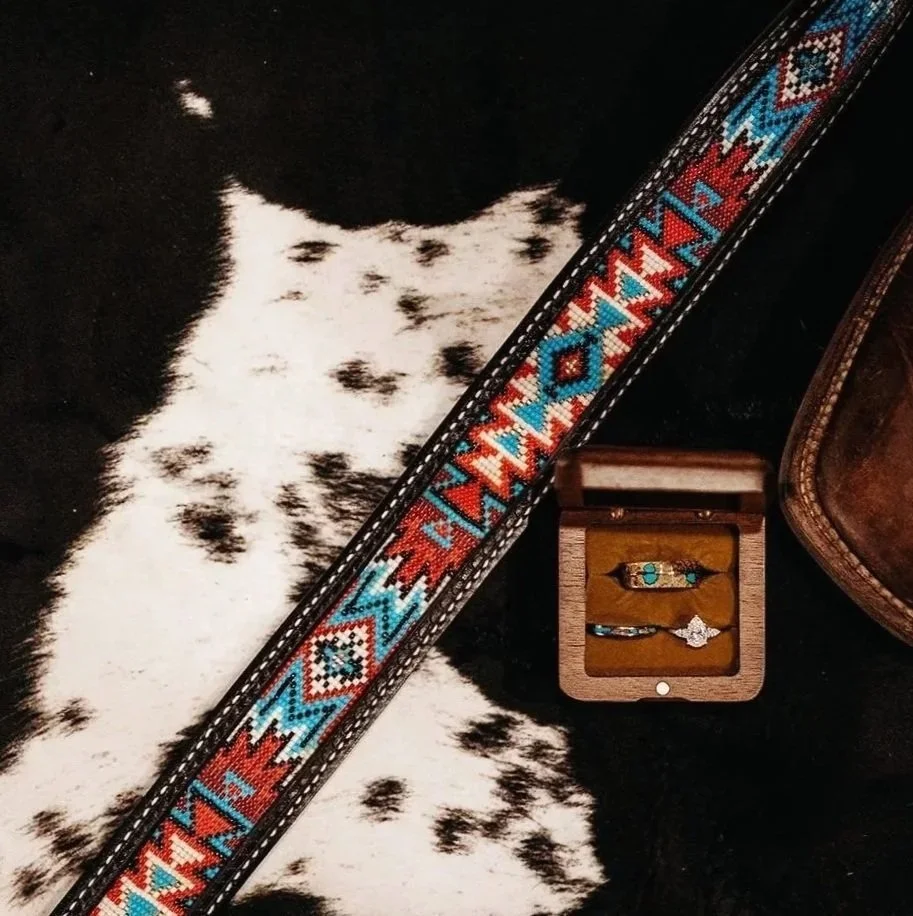 A beaded belt with colorful geometric patterns, jewelry in a wooden box, and part of a brown leather item on a black and white spotted fur surface.