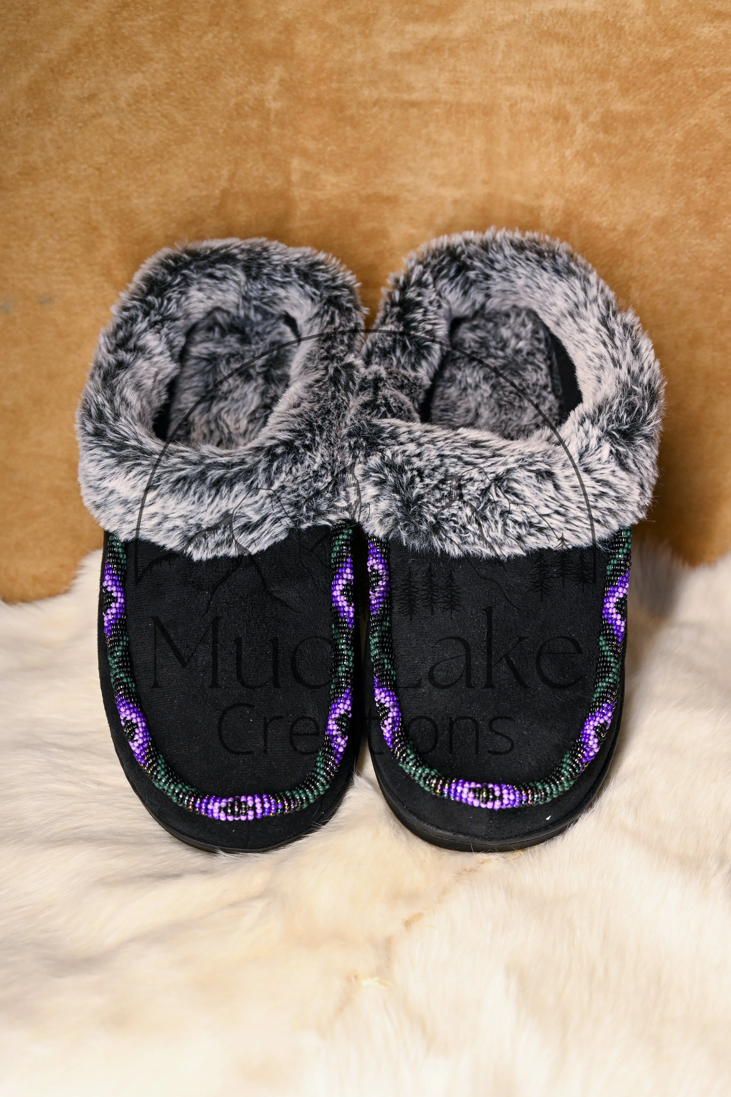 Black moccasins with faux fur trim and colorful beaded accents over a white furry surface.