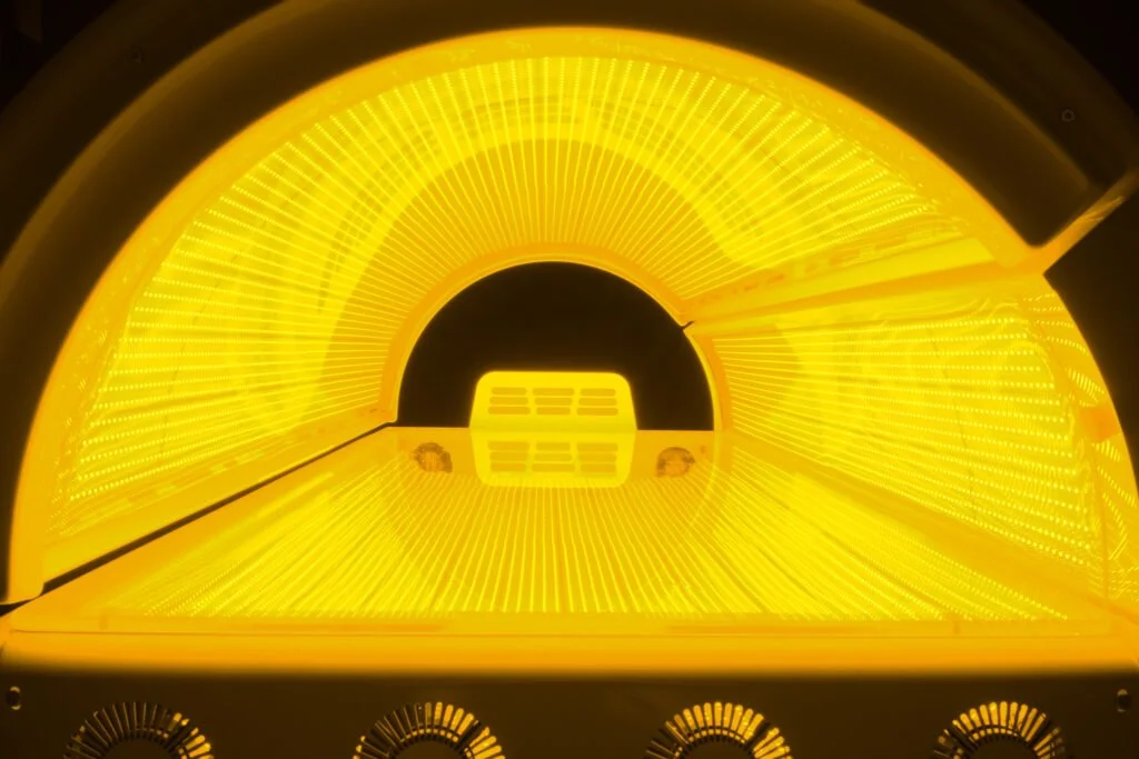 Close-up of a yellow tanning bed with bright internal UV light tubes at Infinity Fitness Studios in Reno