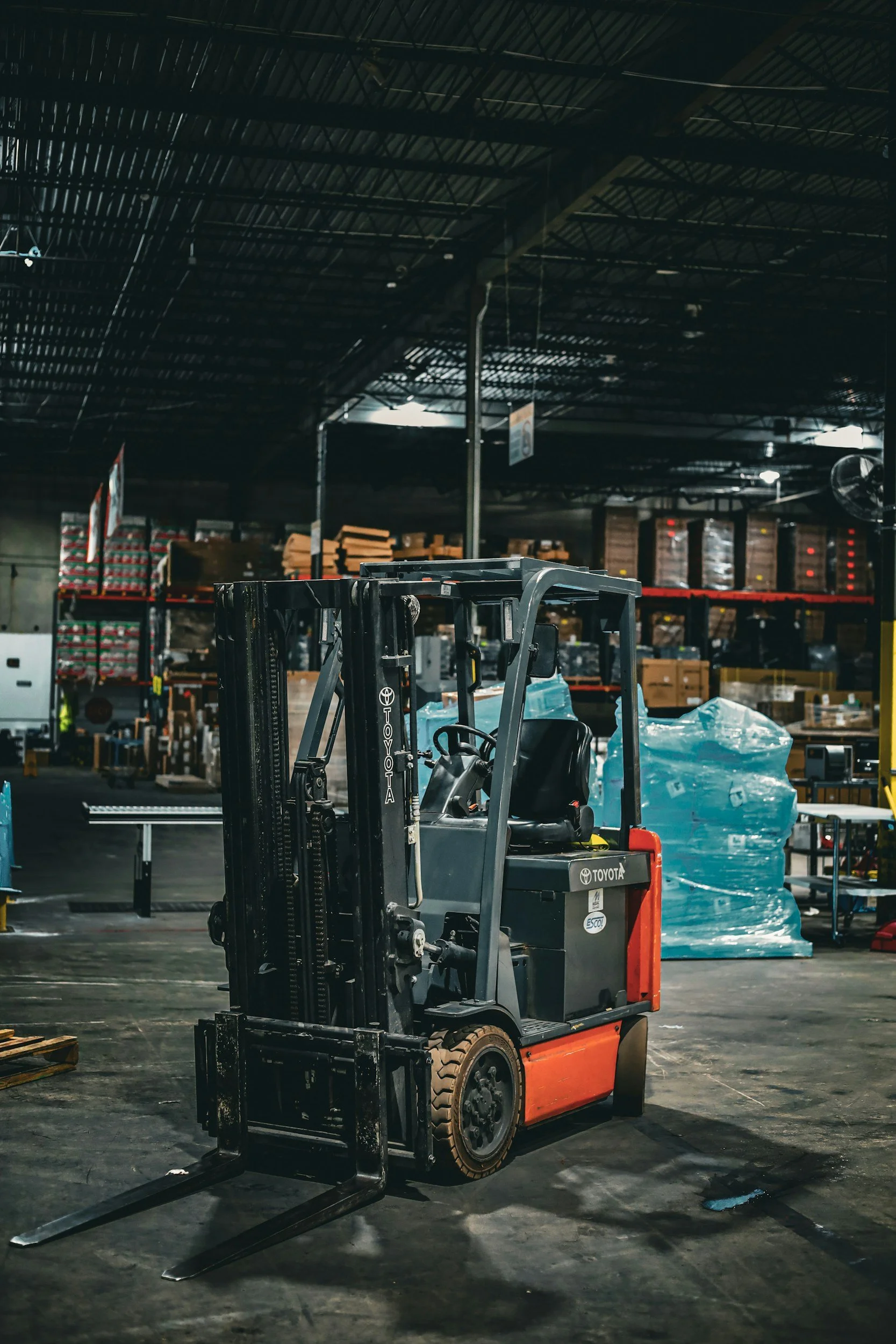 An industrial warehouse with a forklift in the foreground, surrounded by shelves filled with boxes and goods.