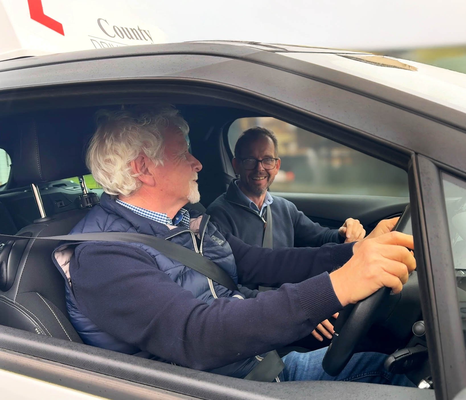 Jim Doyle teaching a lesson on becoming a driving instructor. The two men are sat in the car talking.