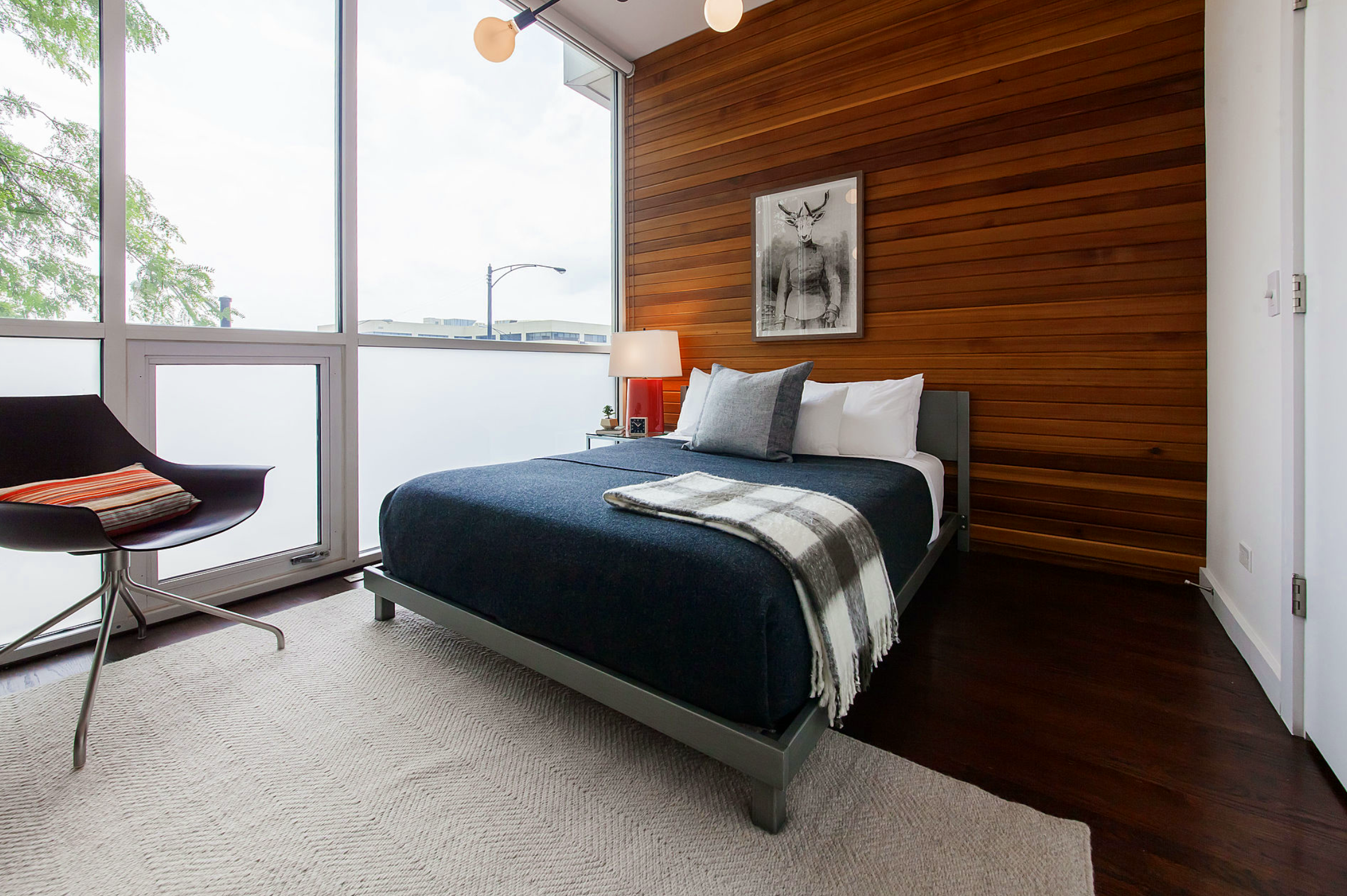 Wicker Park bedroom with wood-paneled walls, modern art, and full-height windows—an intimate retreat blending warmth, texture, and contemporary style.