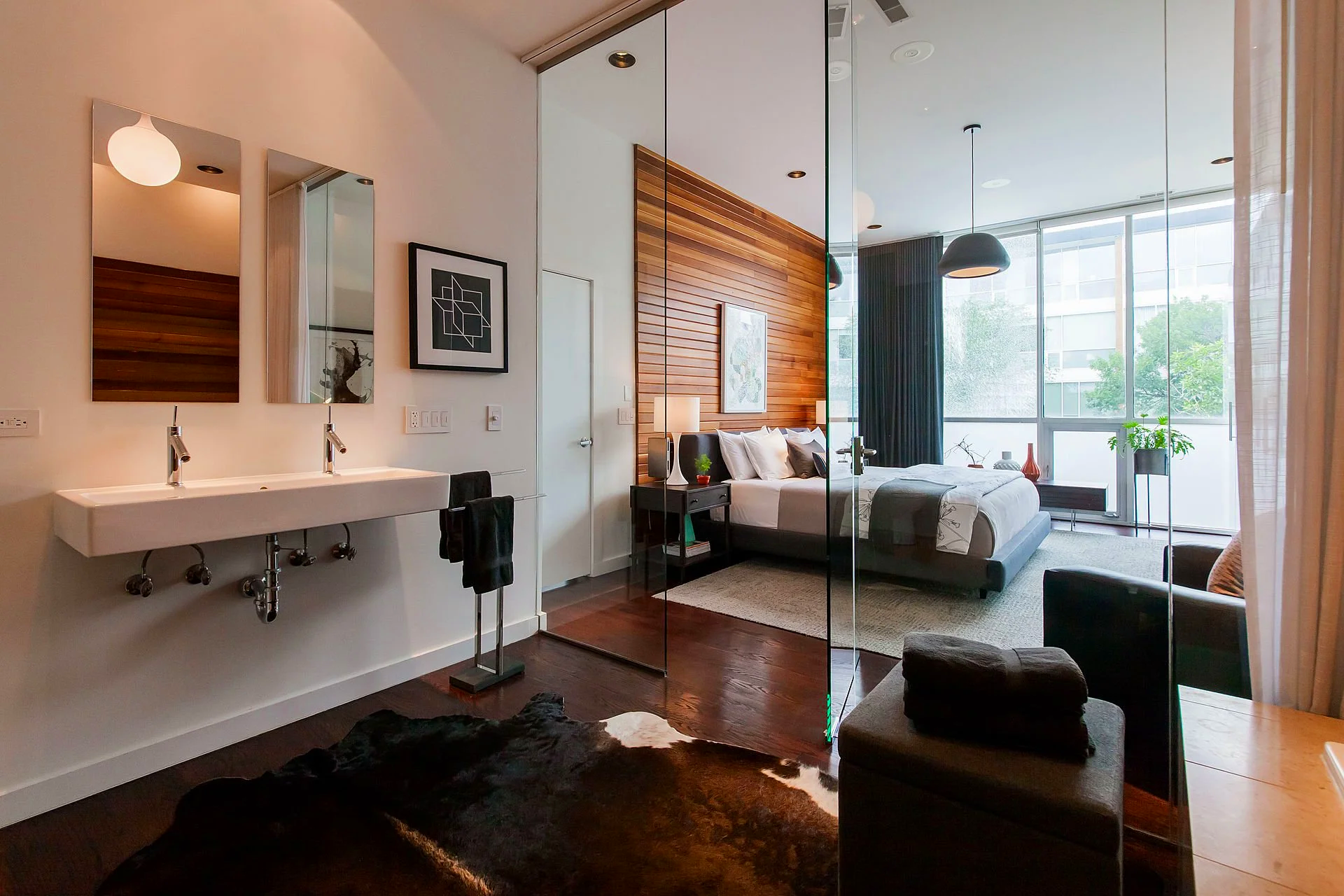 Sleek bathroom with glass partition opening into a wood-accented Wicker Park bedroom, uniting modern functionality with warm, layered design.