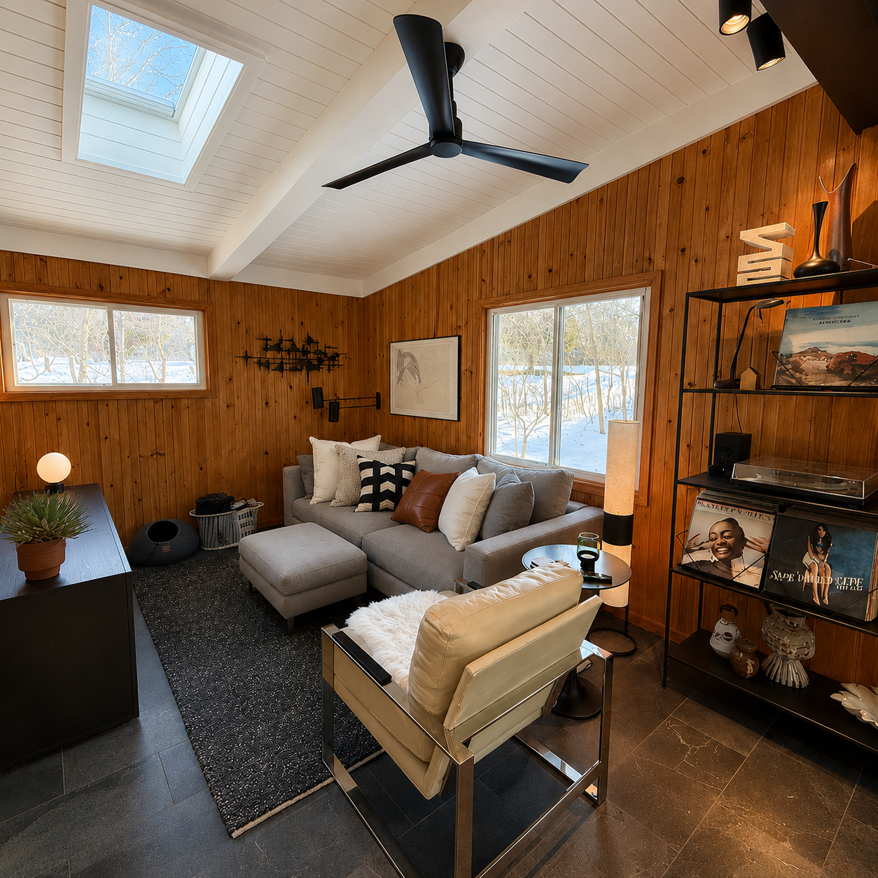 Wood-paneled living room with black metal shelving, skylight, and ceiling fan — Fennville mid-century interior