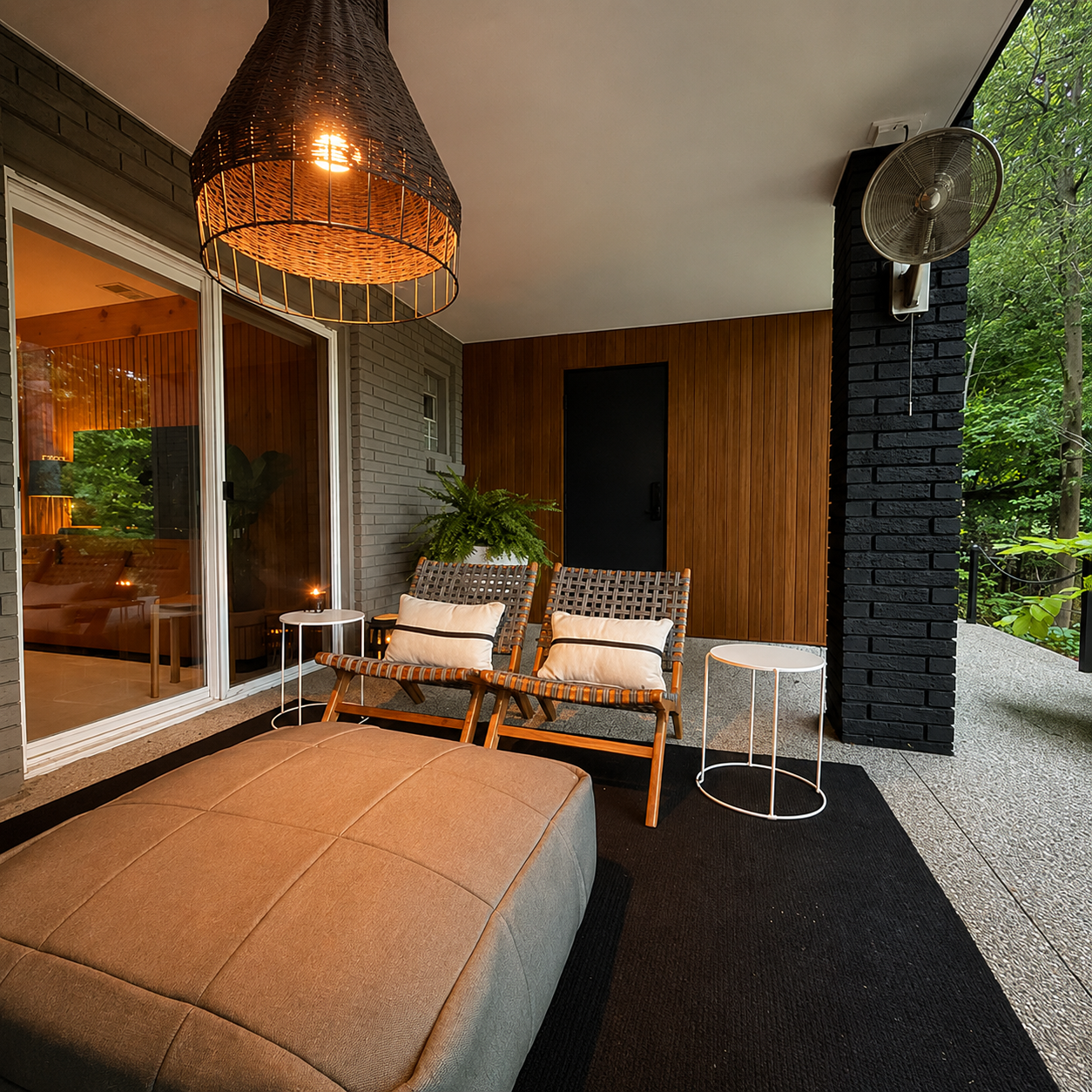 A sophisticated covered patio that seamlessly extends the home's modern design outdoors. Warm wood accents, sculptural lighting, and comfortable lounge seating create an inviting space for year-round relaxation, surrounded by the beauty of the natura