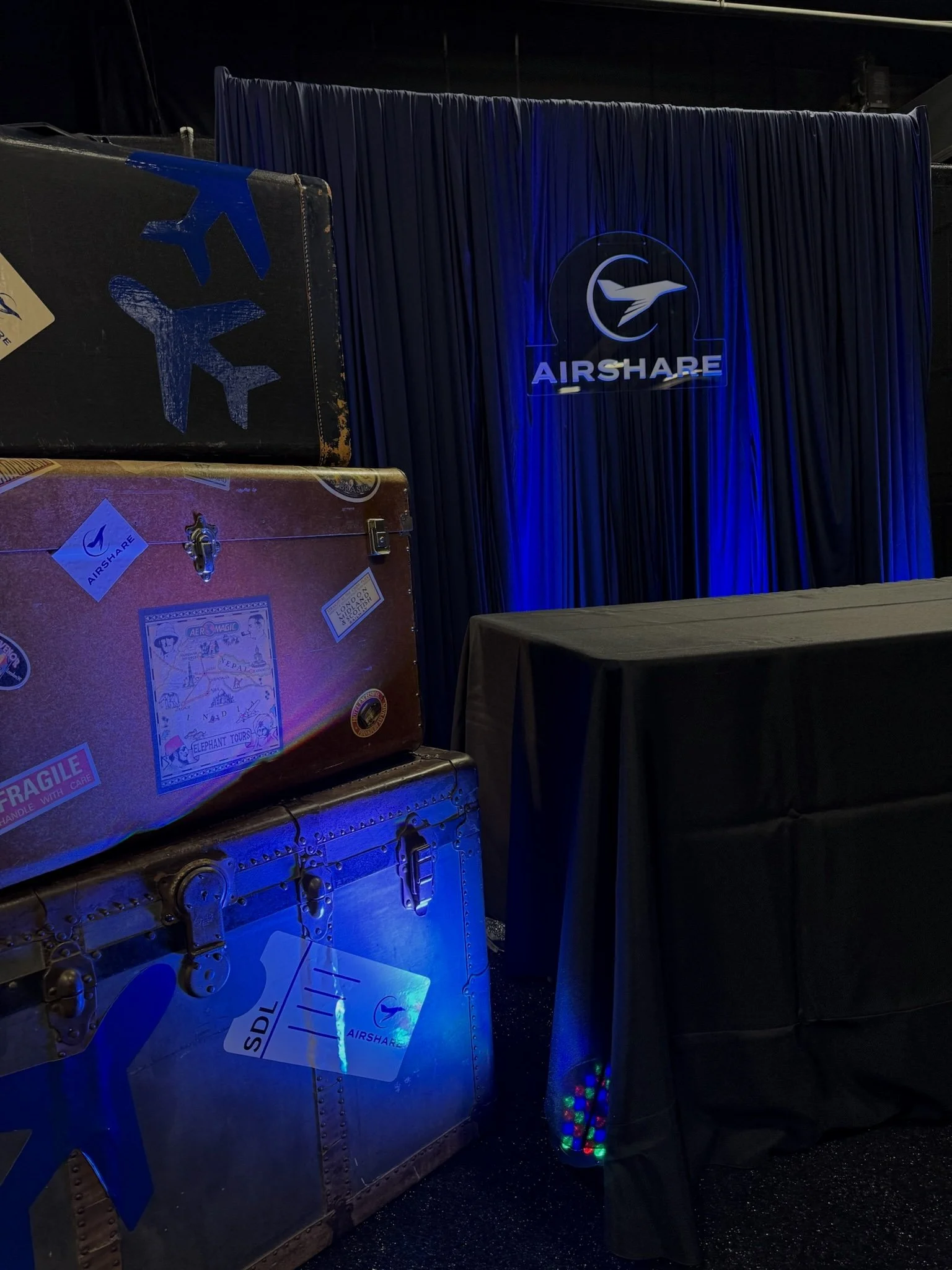 Luxury corporate event installation featuring custom navy blue pipe and drape, branded Airshare signage, aviation-inspired vintage luggage décor, and professional event styling. Designed for conferences, trade shows, networking receptions, VIP lounge
