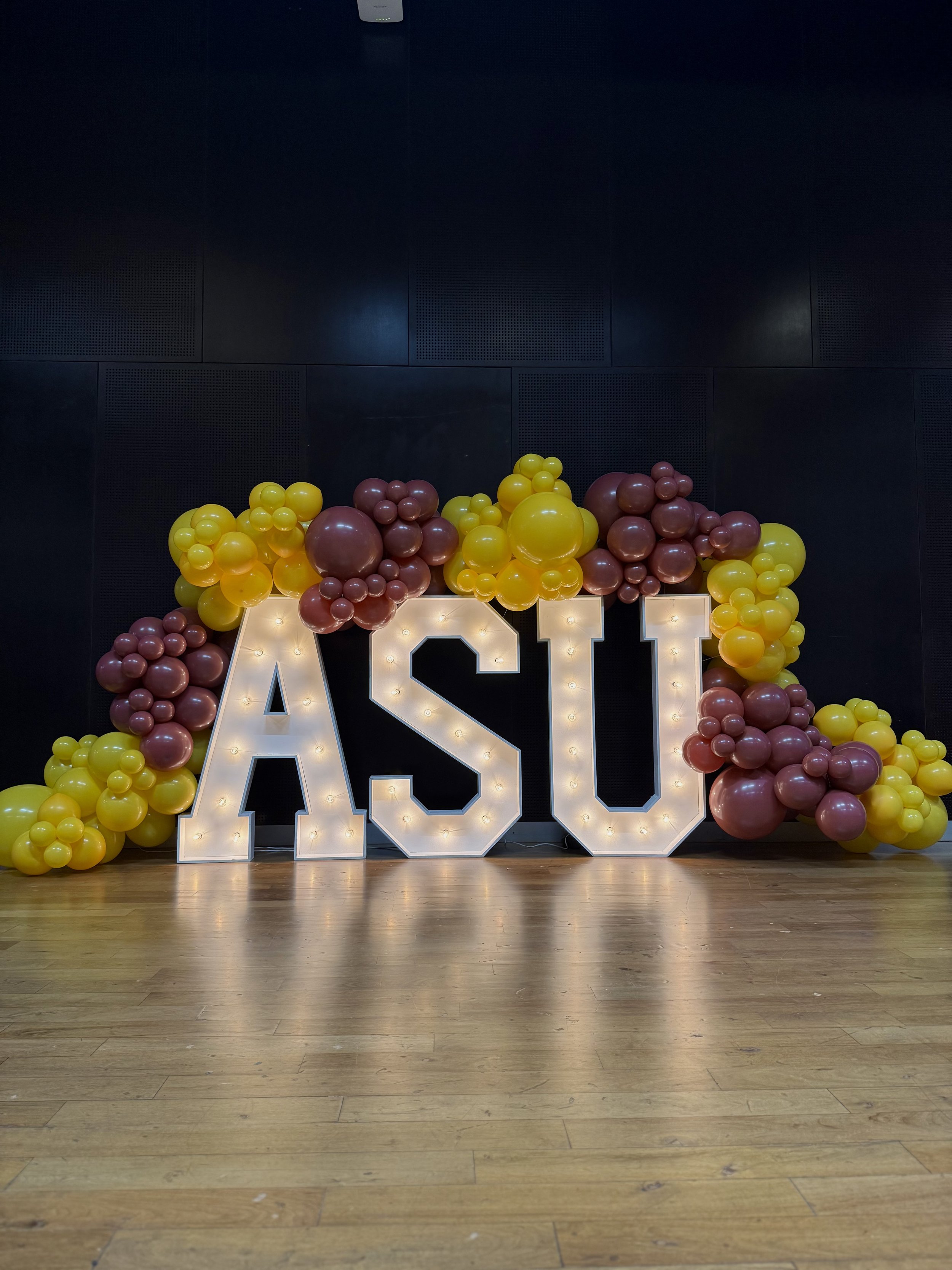 Custom ASU event backdrop featuring illuminated marquee letters and organic maroon and gold balloon garlands. This eye-catching installation creates a memorable photo opportunity for Arizona State University graduations, student events, alumni gather