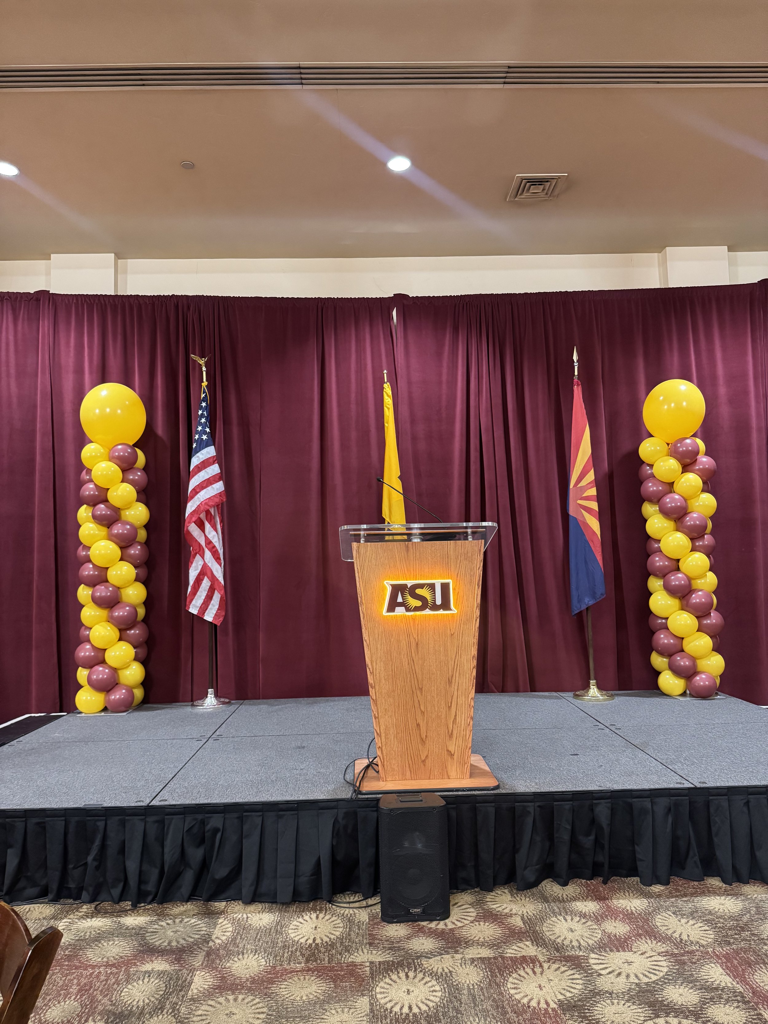 Custom ASU event décor featuring maroon stage draping, organic gold and maroon balloon columns, and Arizona State University branding. Designed for commencement ceremonies, awards presentations, academic conferences, student events, and university ce