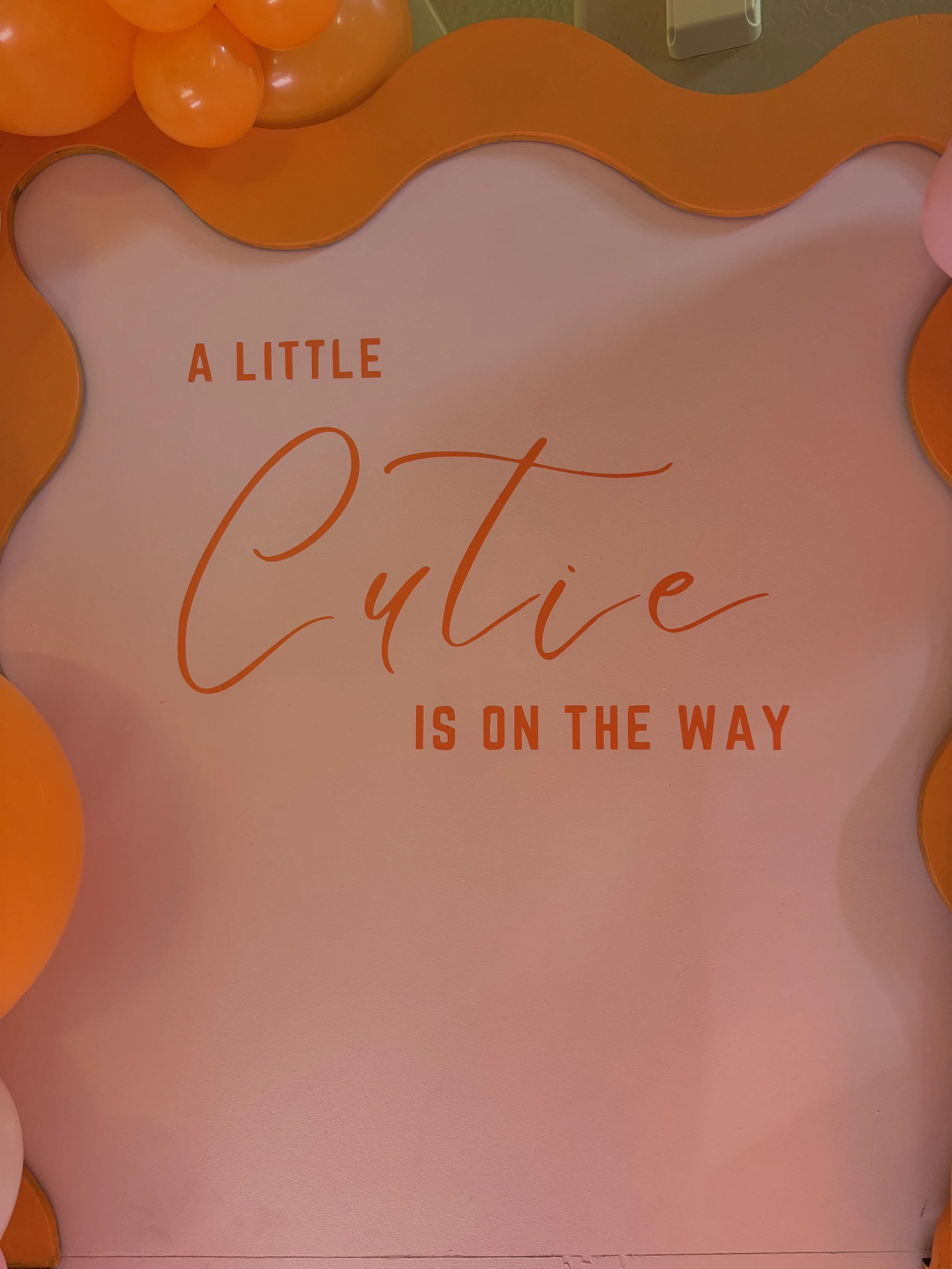 Custom "A Little Cutie Is On The Way" baby shower backdrop featuring a modern wavy panel design with vibrant orange balloon décor inspired by a citrus and cutie orange theme. This stylish baby shower photo backdrop creates the perfect focal point for