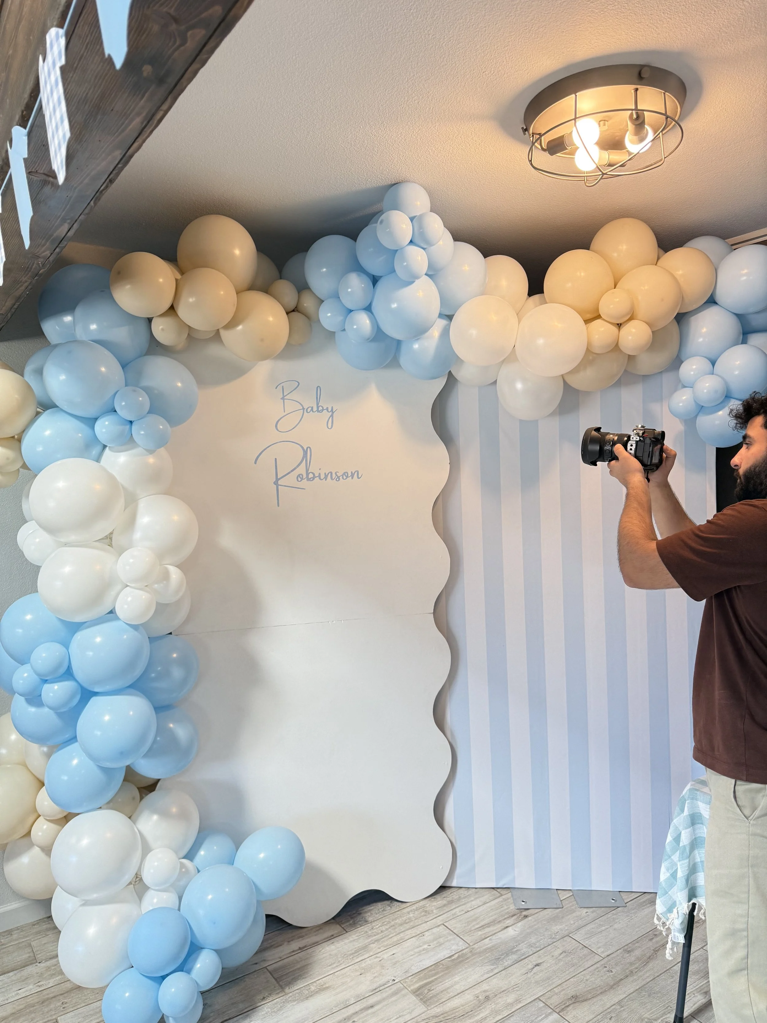 Luxury baby shower backdrop featuring custom wavy panels, soft blue and white organic balloon garlands, and personalized "Baby Robinson" signage. Designed with elegant pastel tones and modern event styling, this custom baby shower installation create