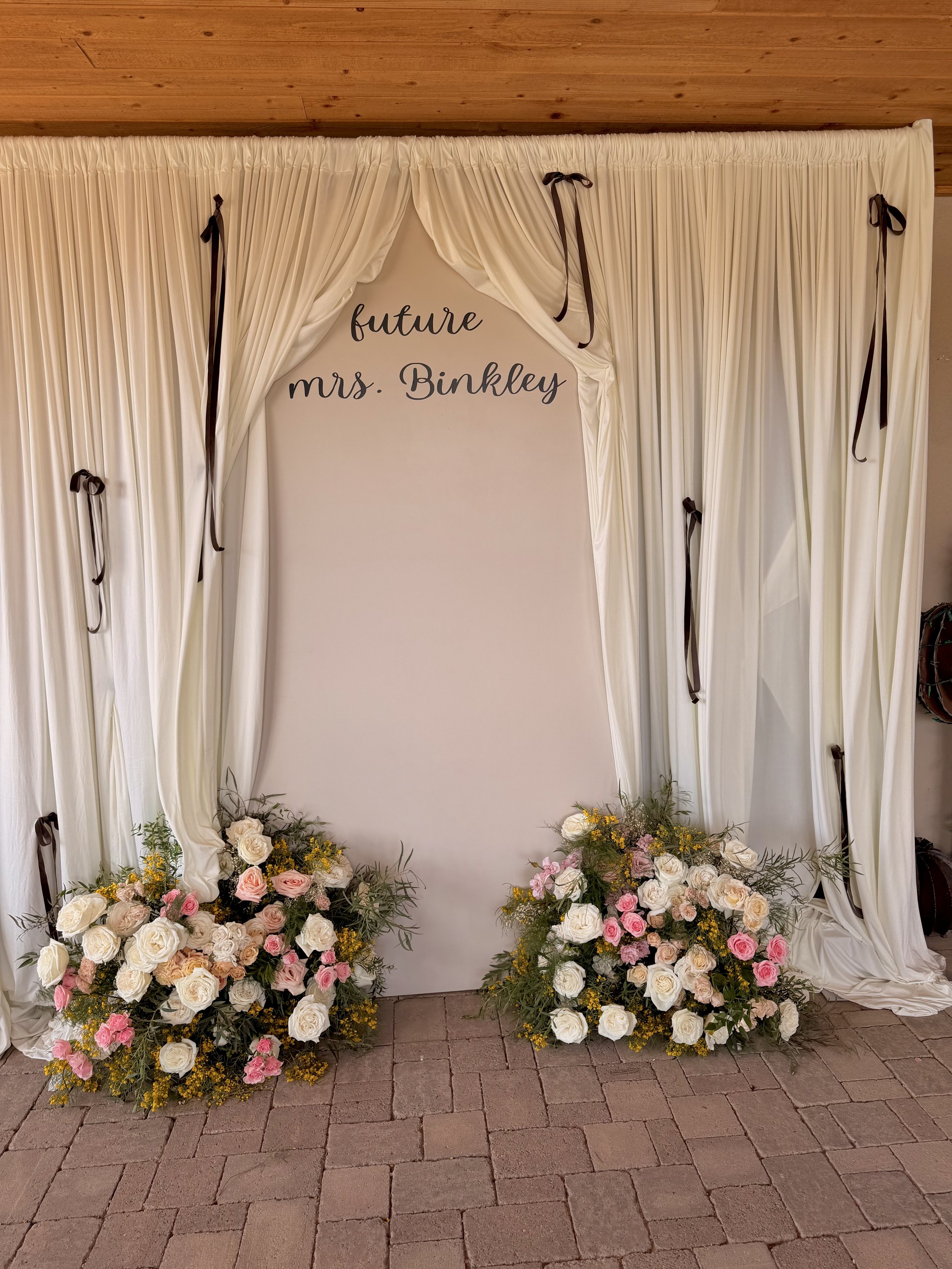 Luxury bridal shower backdrop featuring custom ivory draping, romantic garden-style floral arrangements, and personalized "Future Mrs. Binkley" signage. Designed with soft neutral tones, elegant gathered fabric panels, and lush blush and ivory floral