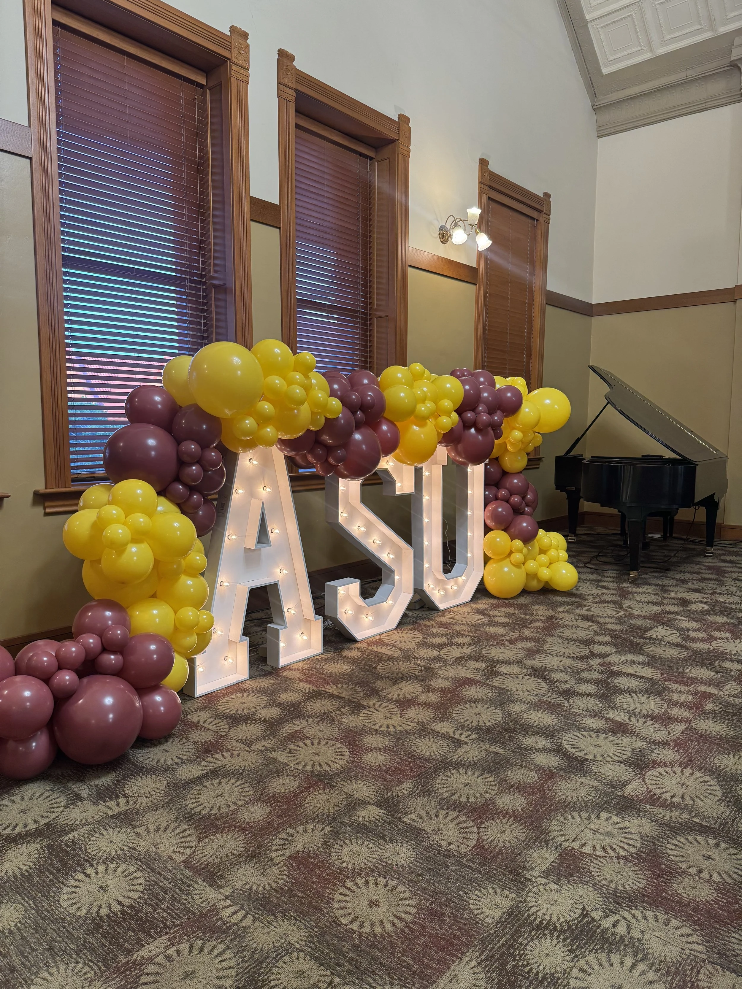 Custom Arizona State University event décor featuring illuminated ASU marquee letters surrounded by organic maroon and gold balloon garlands. Designed for graduations, recruitment events, campus celebrations, alumni gatherings, and university activat