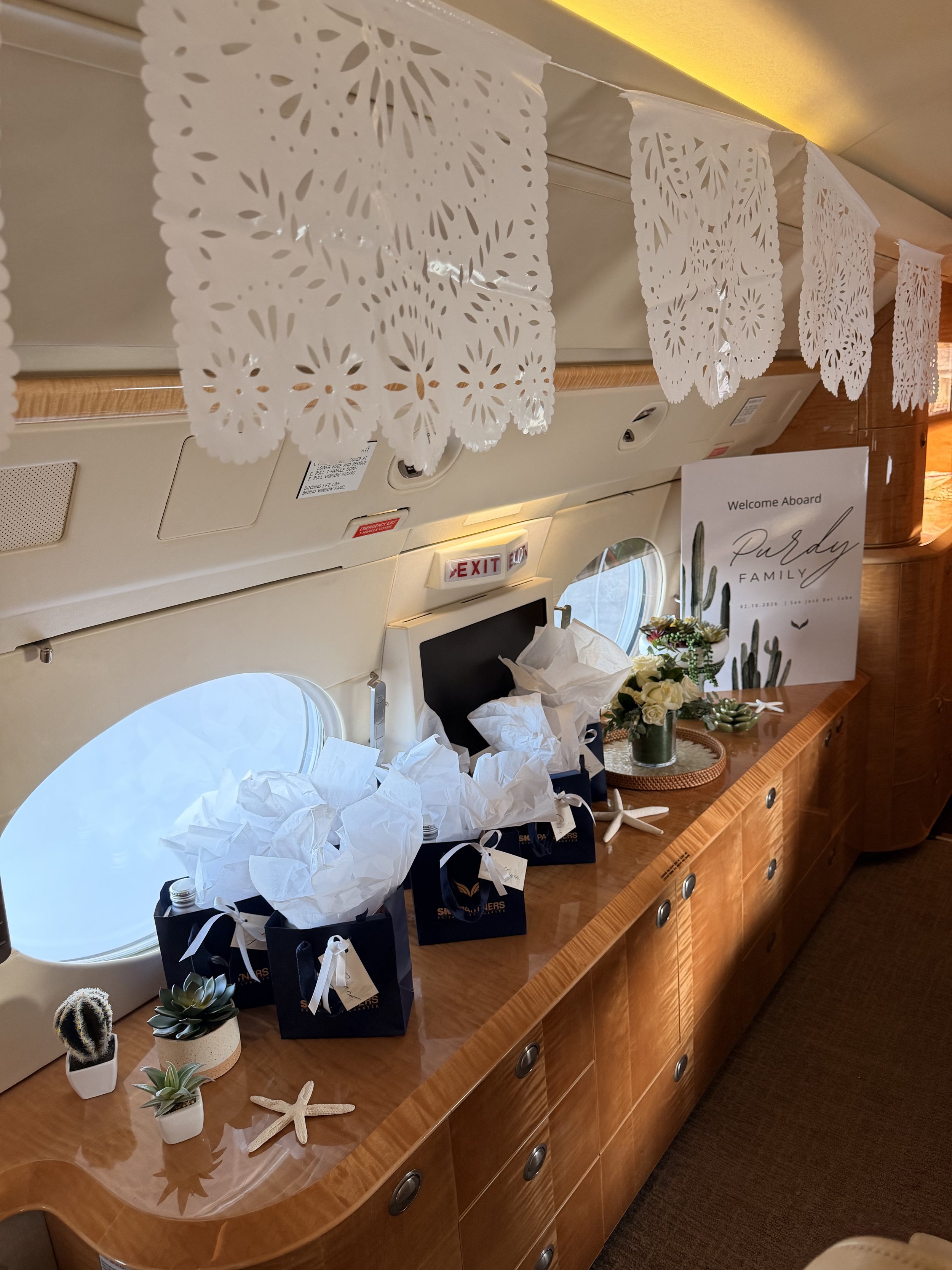 Custom private jet event styling featuring elegant floral arrangements, curated guest welcome gifts, decorative papel picado accents, and luxury travel-inspired details. Designed for VIP experiences, destination celebrations, corporate travel events,