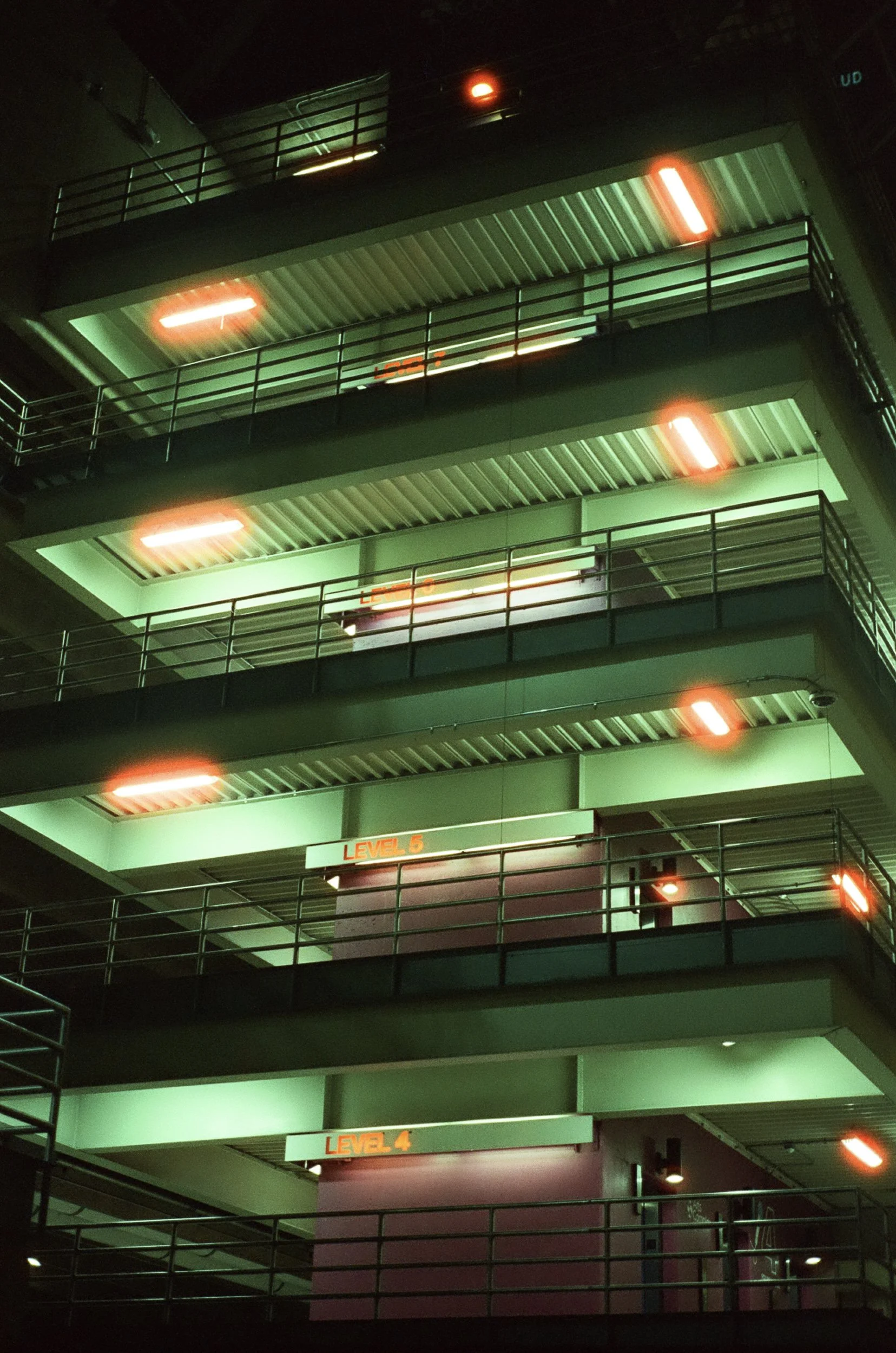 Multiple levels of a parking garage at night, with illuminated signs indicating 'Level 4' and 'Level 5'. The structure is lit with green and red lights.