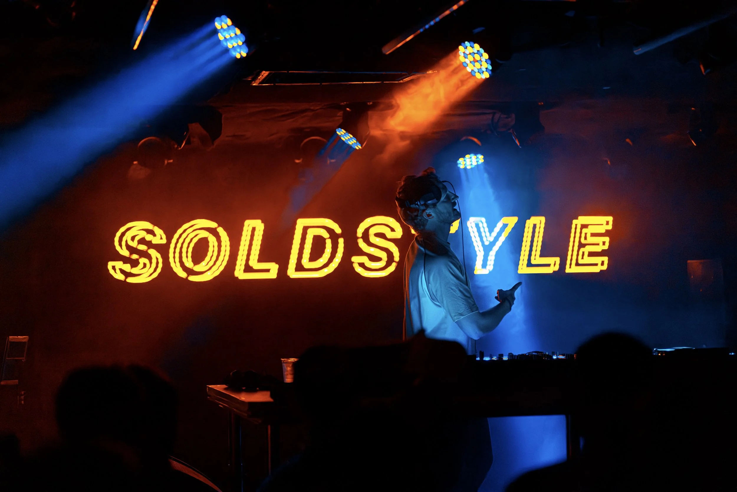 A DJ performs at a nightclub with colorful neon lights and a sign that reads 'SOLD'.