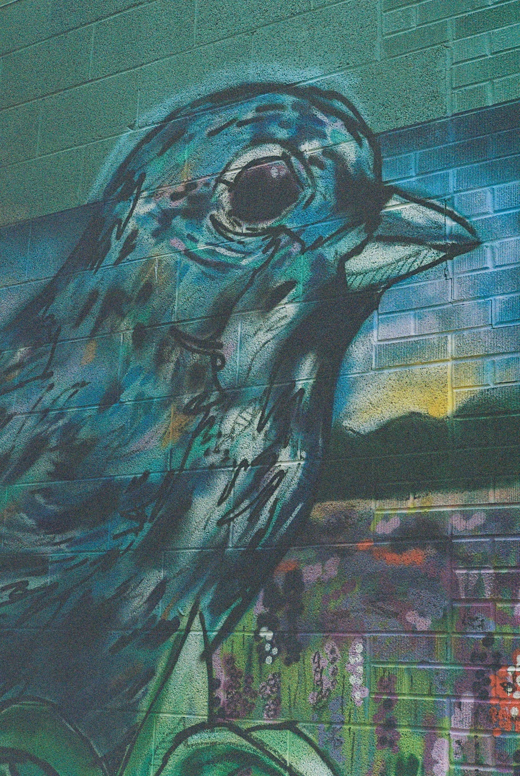 Colorful street art mural of a screaming face on a brick wall, with vibrant blues, greens, pinks, and purples.