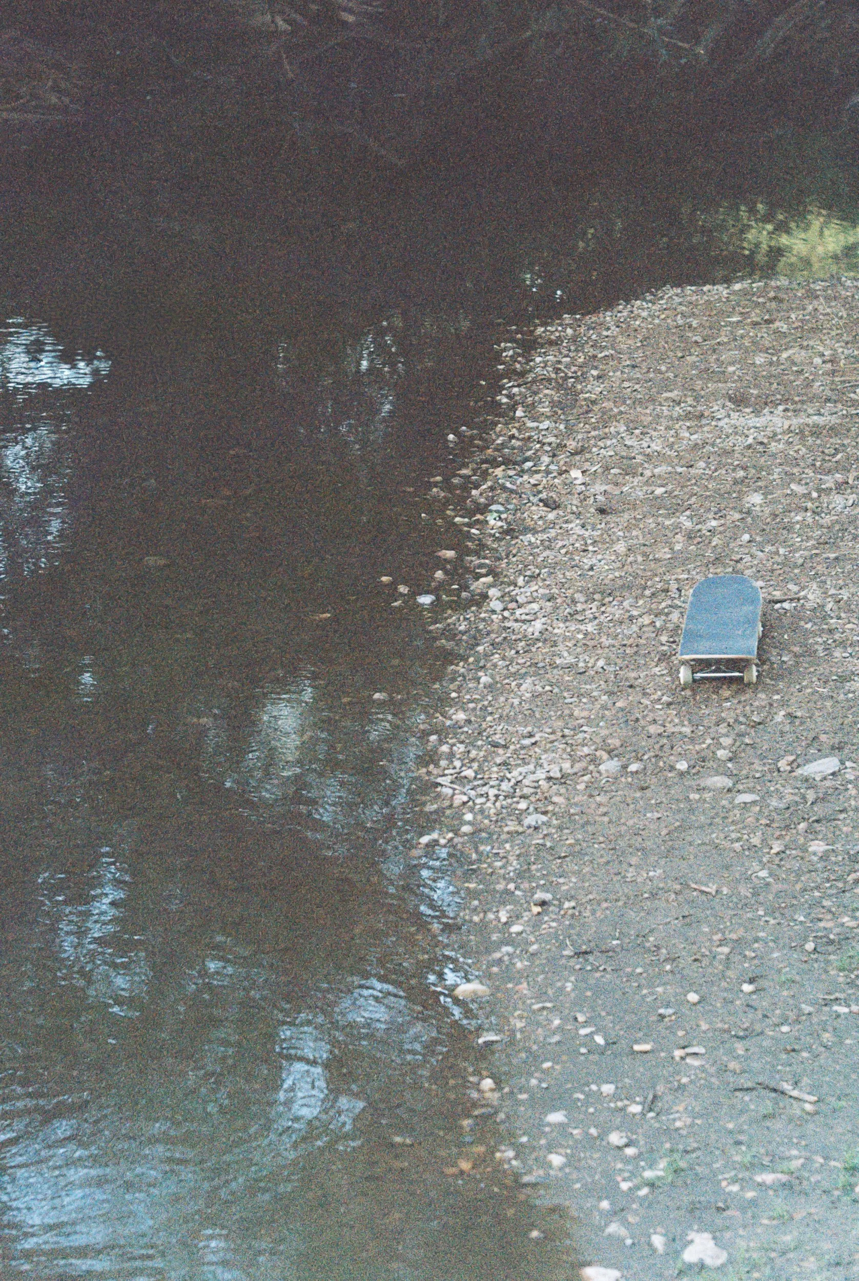 A small boat with a blue cover on a rocky shore beside a dark river with overhanging trees.
