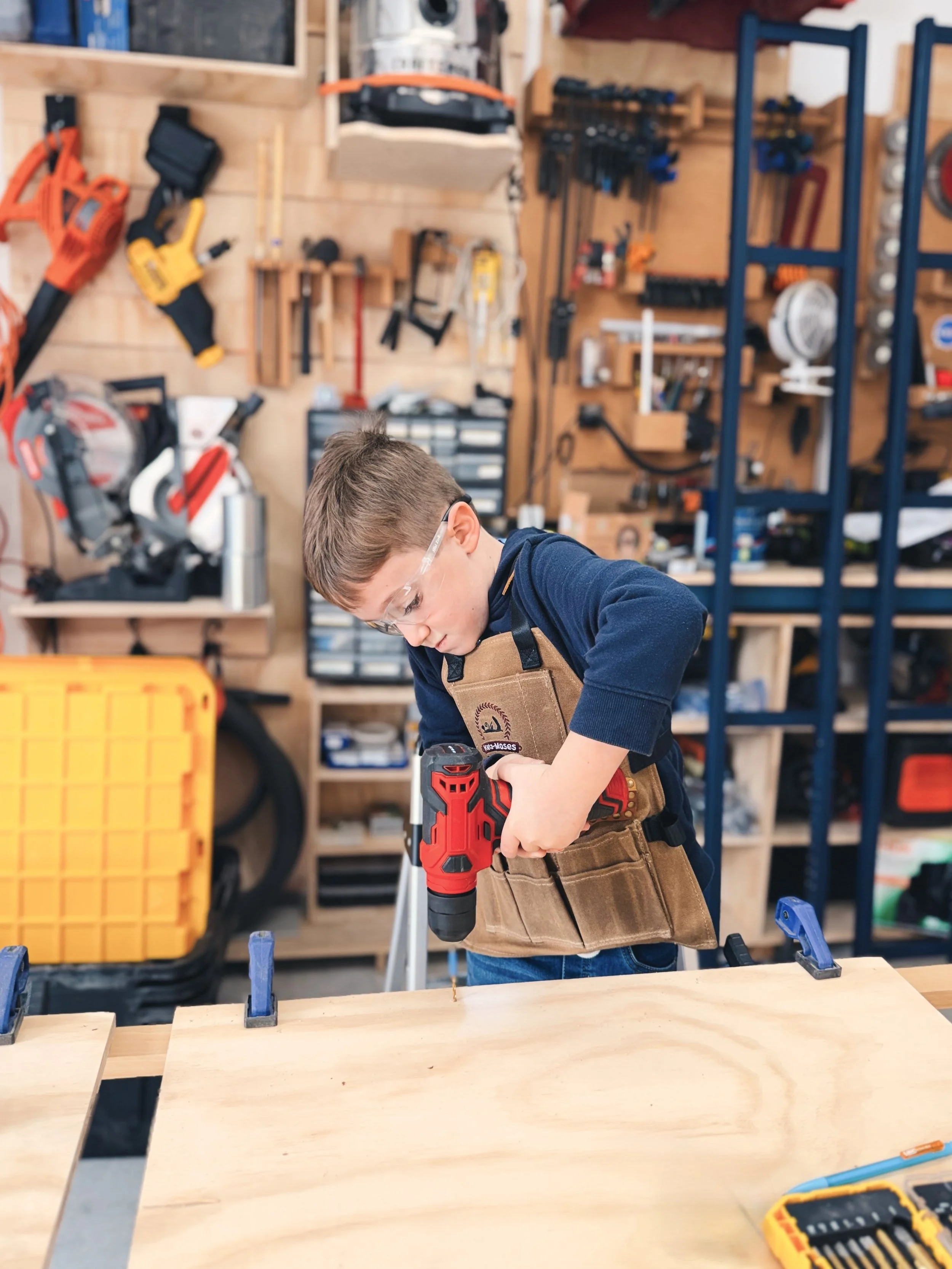 Small child wearing a kids KM Tools apron works in a shop