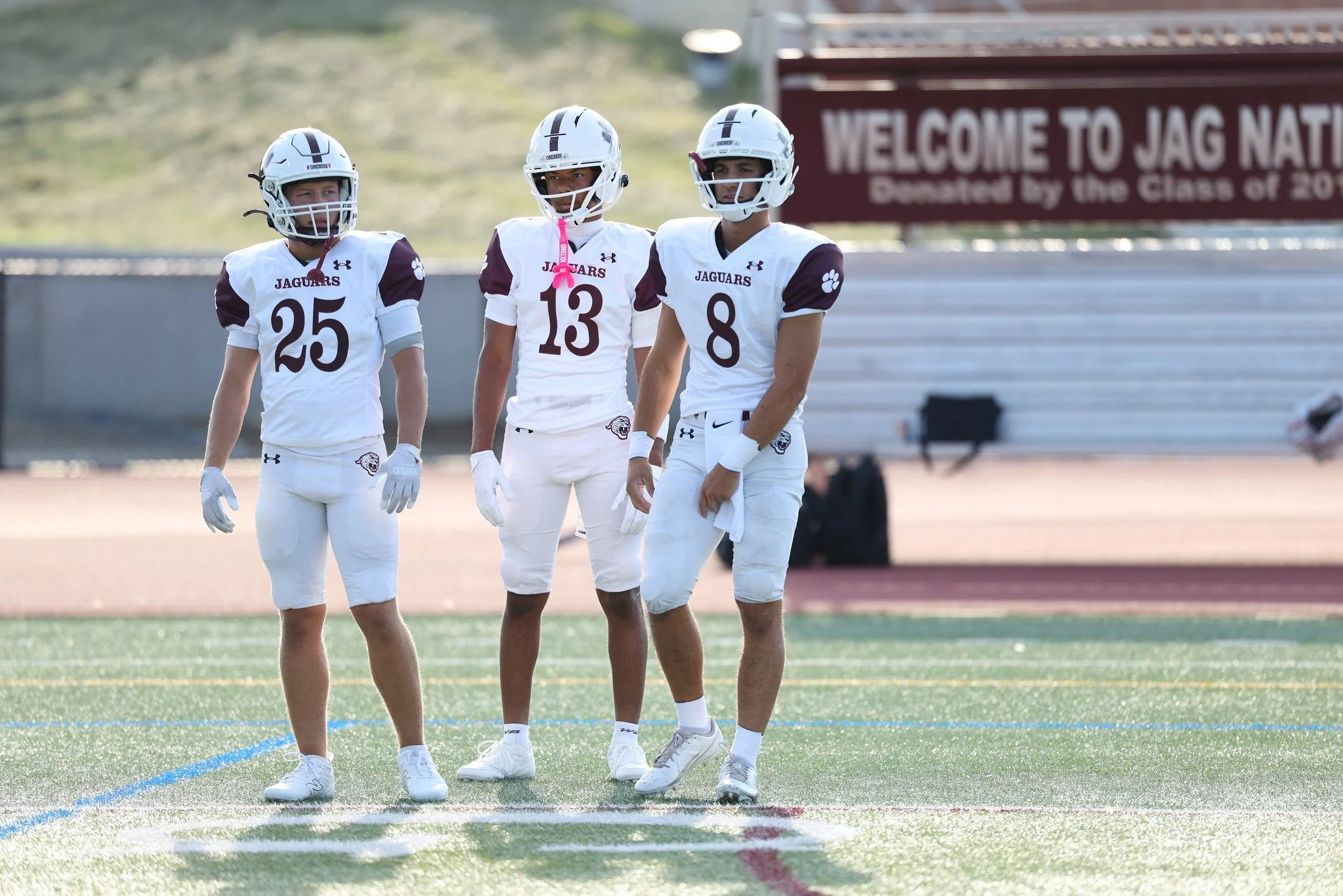 Football team called Jaguars practicing on the field with players in maroon jerseys and white pants, with a crowd of spectators in the stands.